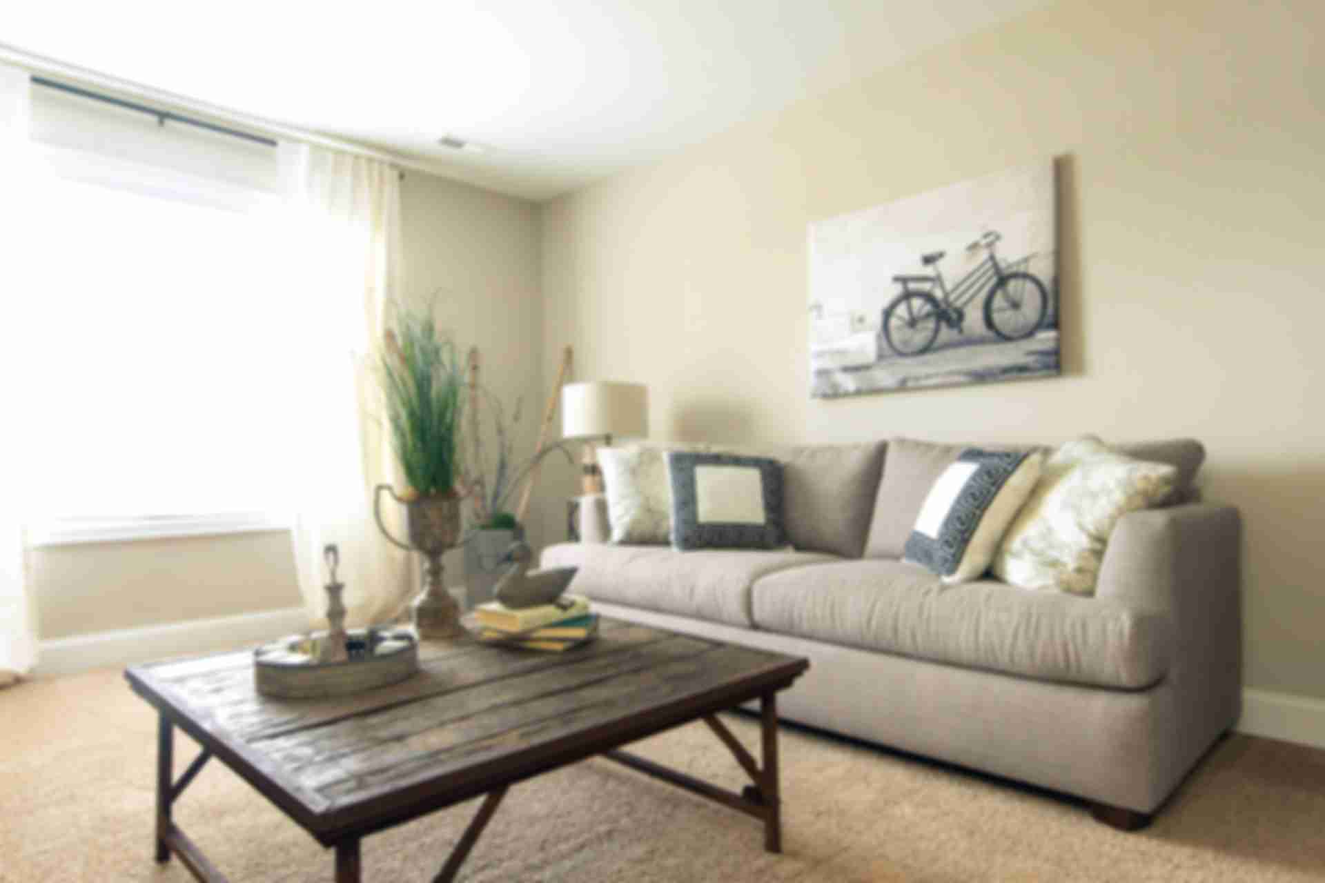 Cozy living room at Summer Pointe in Madison Alabama with beige sofa, rustic wood coffee table, bicycle wall art, and natural light