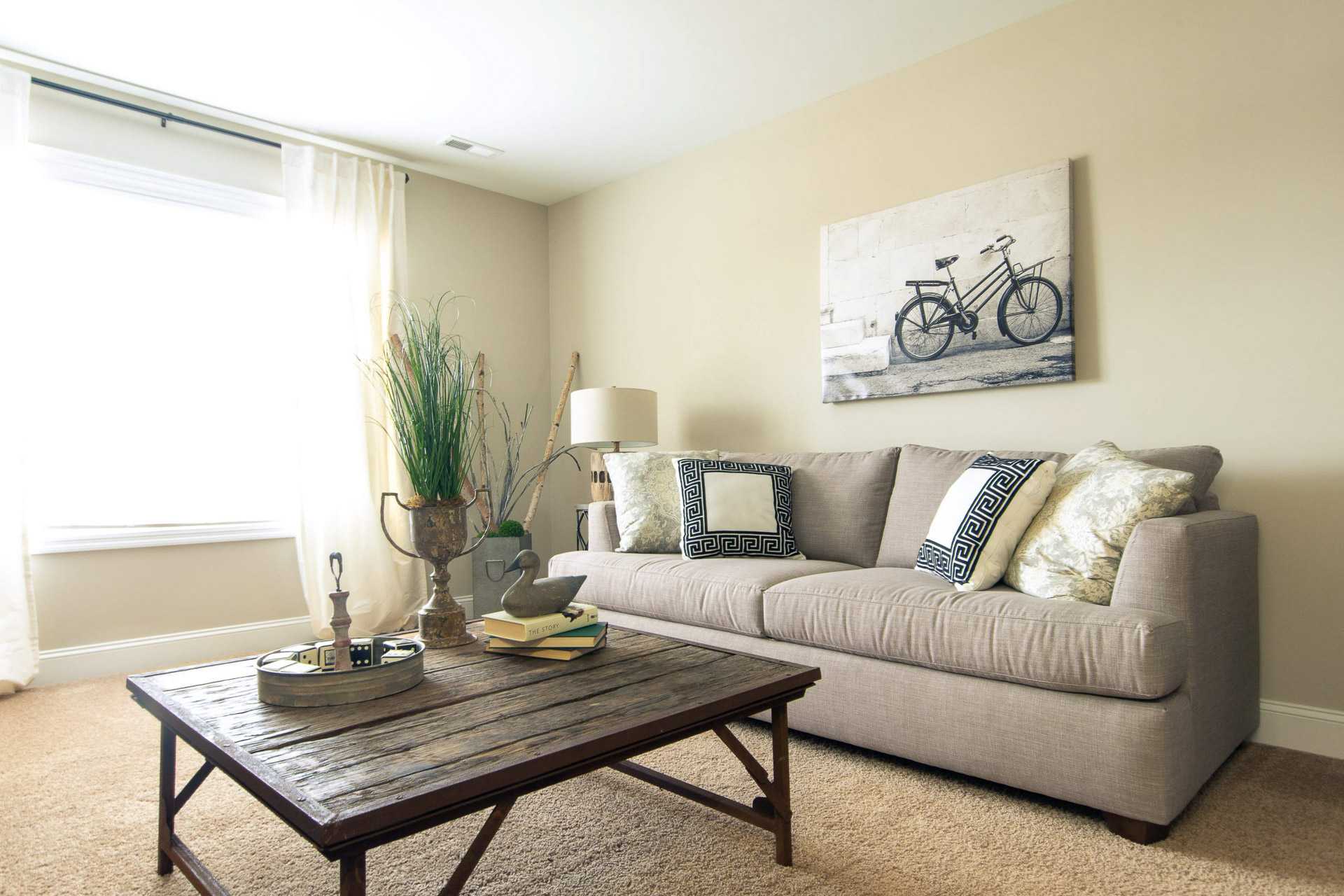 Cozy living room at Summer Pointe in Madison Alabama with beige sofa, bicycle wall art, potted plant, and rustic wood coffee table