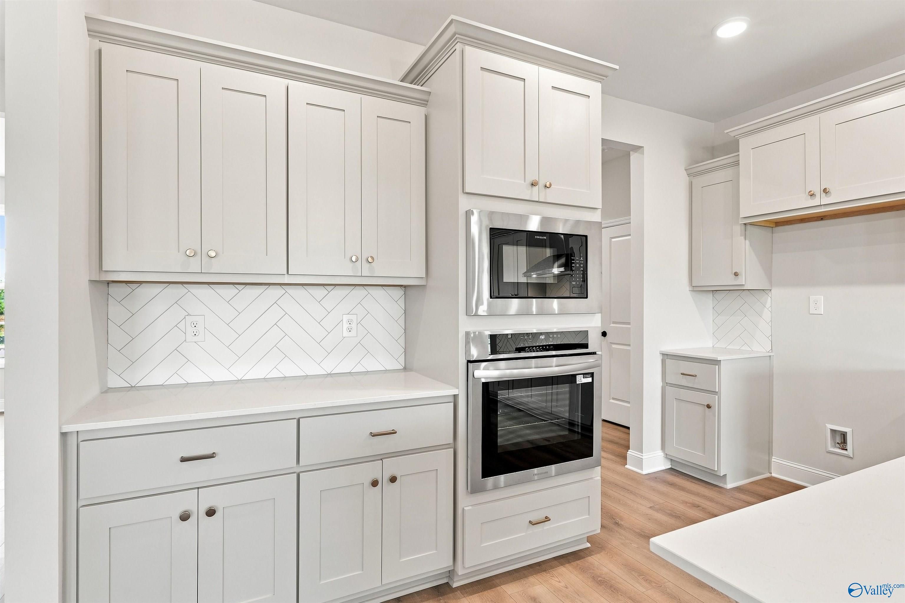 Modern kitchen with light gray cabinets, herringbone backsplash, and stainless appliances in The Oxford, Kendall Farms.