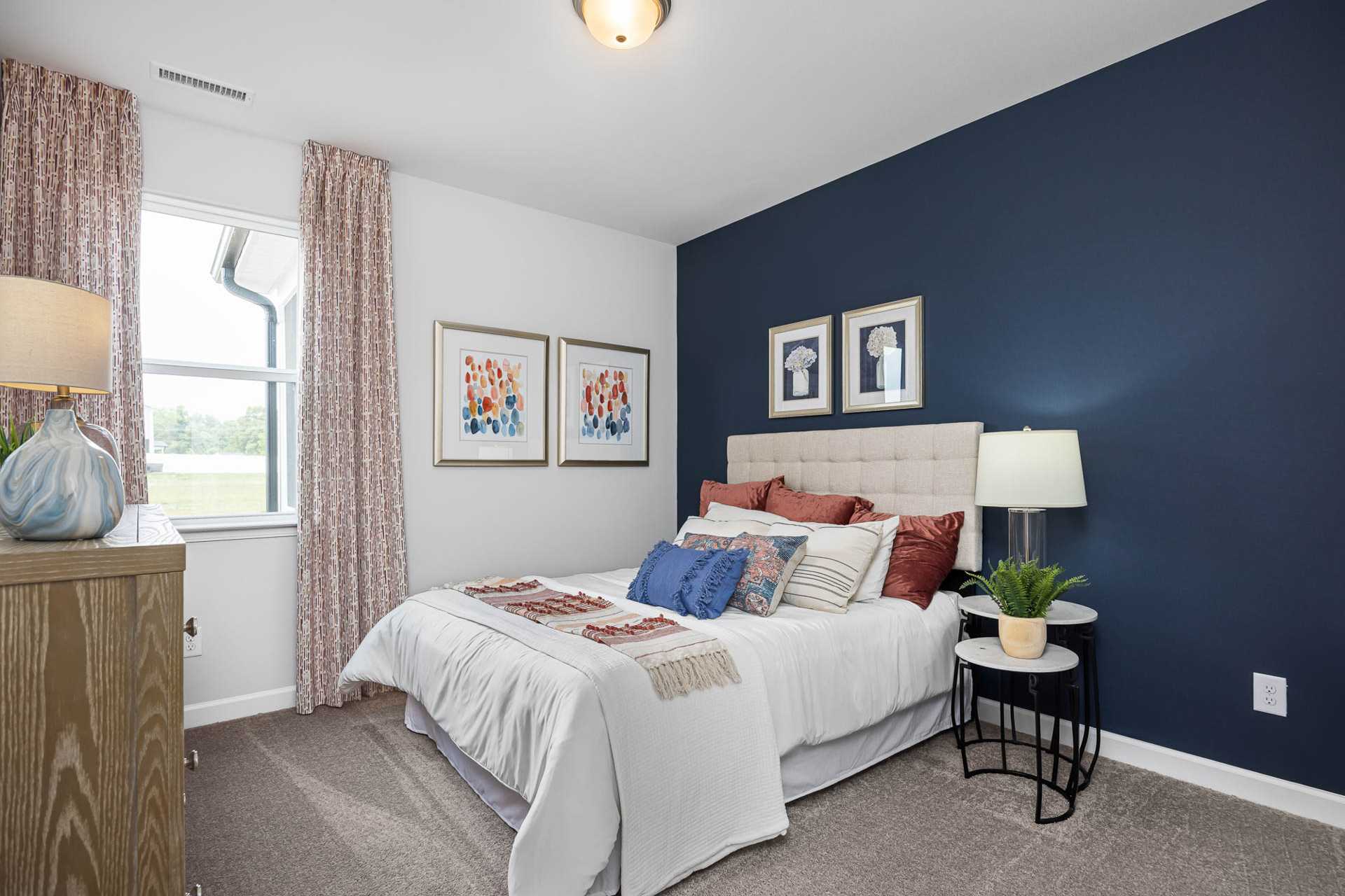 Cozy bedroom with navy accent wall, white bed with colorful pillows, abstract art, and window view at Beverly Place in Four Oaks NC