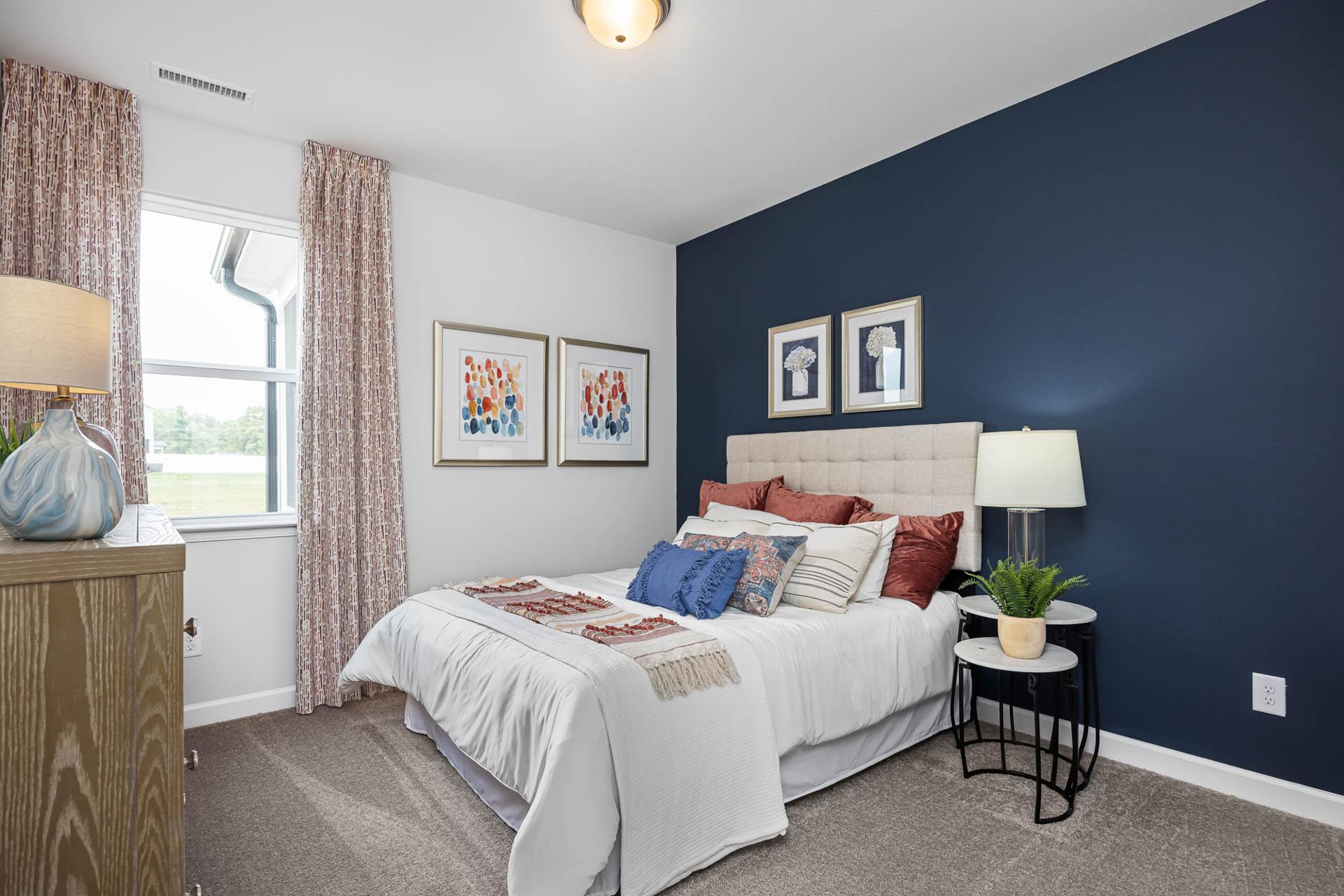 Cozy bedroom with navy accent wall, white bed with colorful pillows, abstract art, and window view at Beverly Place in Four Oaks NC