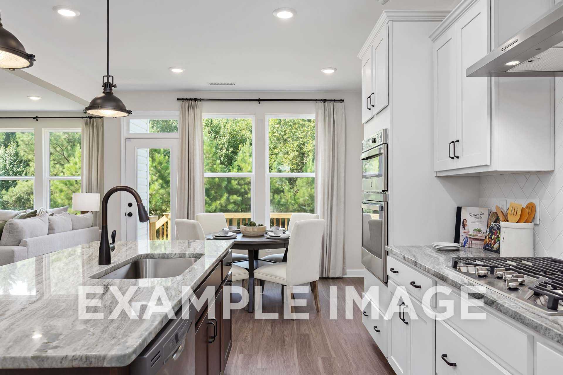 Spacious kitchen in The Willow F with white shaker cabinets, granite island, stainless appliances, and breakfast nook overlooking greenery