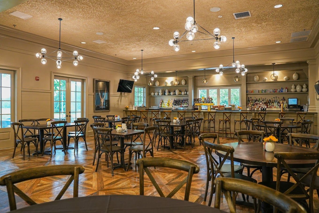 Elegant clubroom bar at Addison West in Holly Springs NC with wooden tables, chairs, pendant lights and stocked shelves