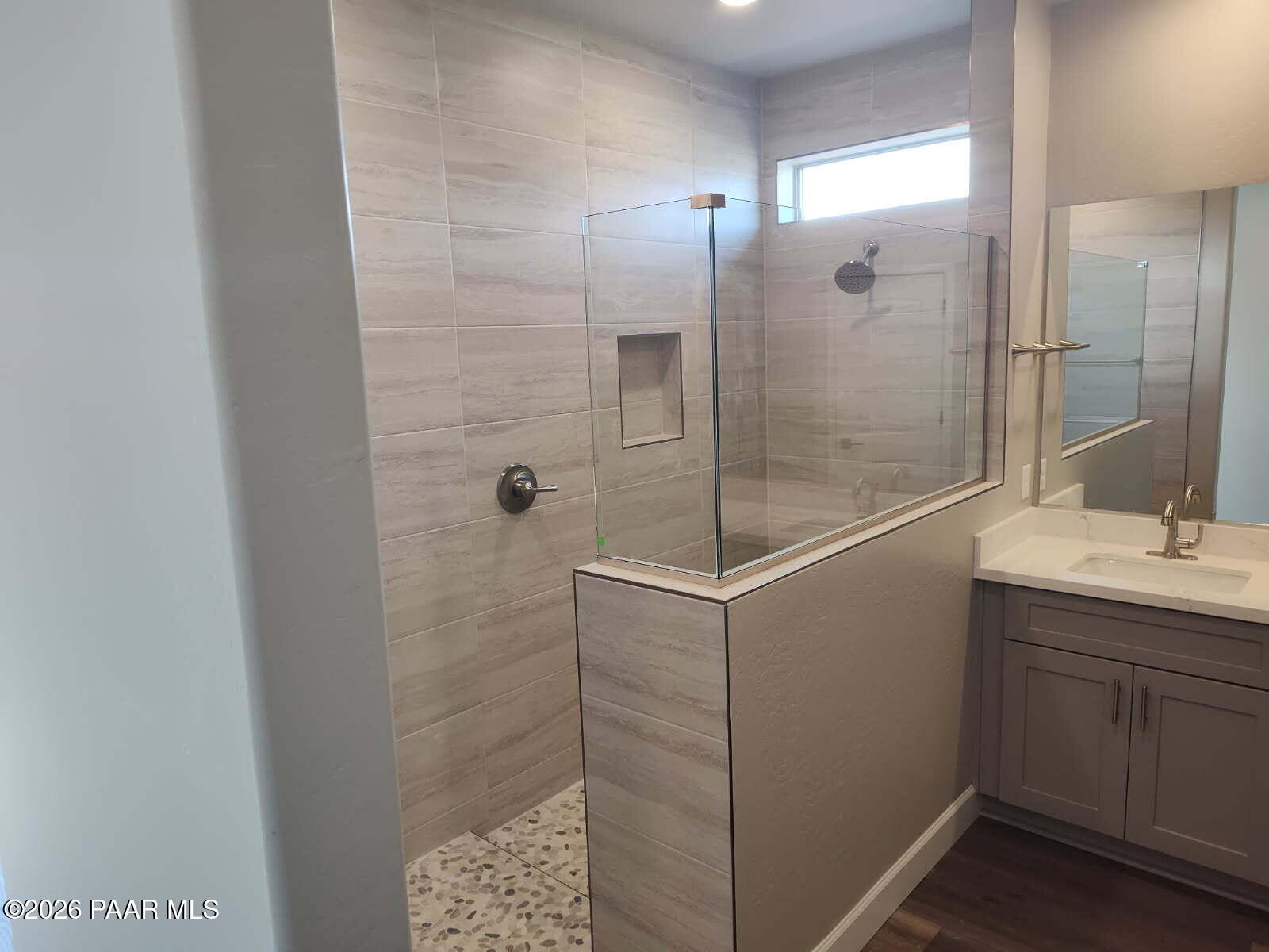 Modern master bathroom featuring frameless glass shower with gray porcelain tile, pebble floor, and quartz vanity in Davidson Homes The Harmony C, Prescott Valley