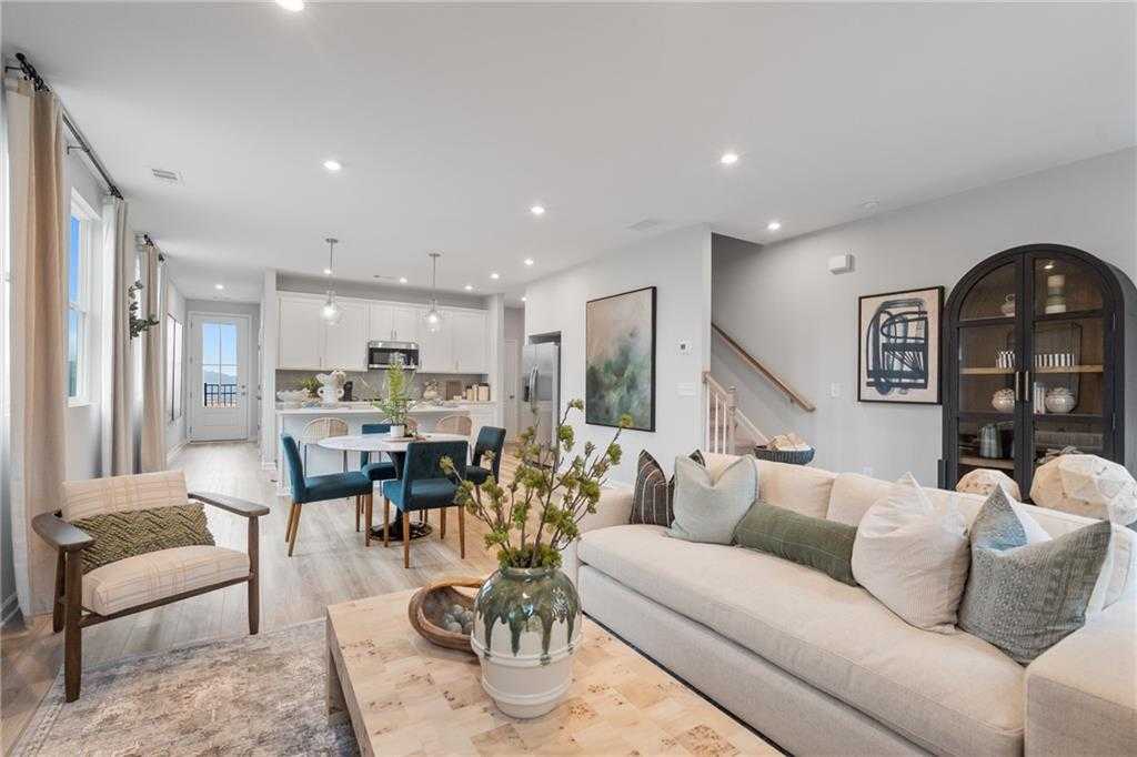 Open-concept living room with beige sofa, wooden coffee table, blue dining chairs in The Wilmington B by Davidson Homes, Emerson, Georgia