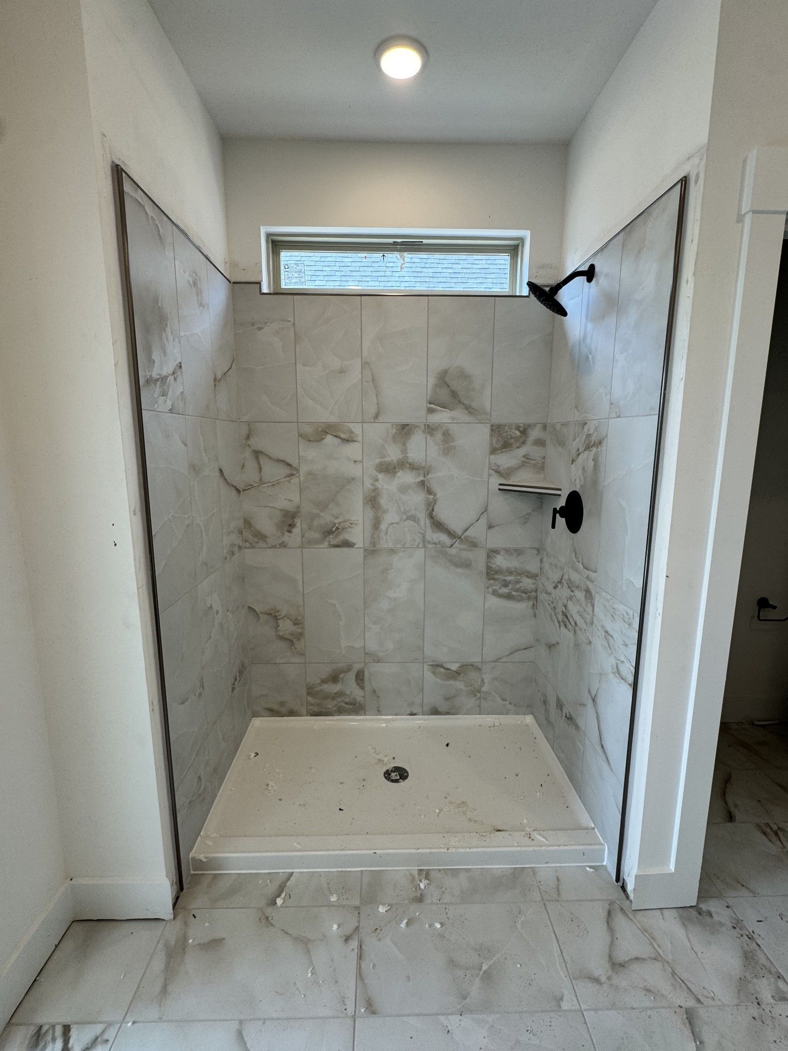 Modern walk-in shower with white marble tiles, rain showerhead, and window in master bath of Davidson Homes Prairie C, Gallatin, TN