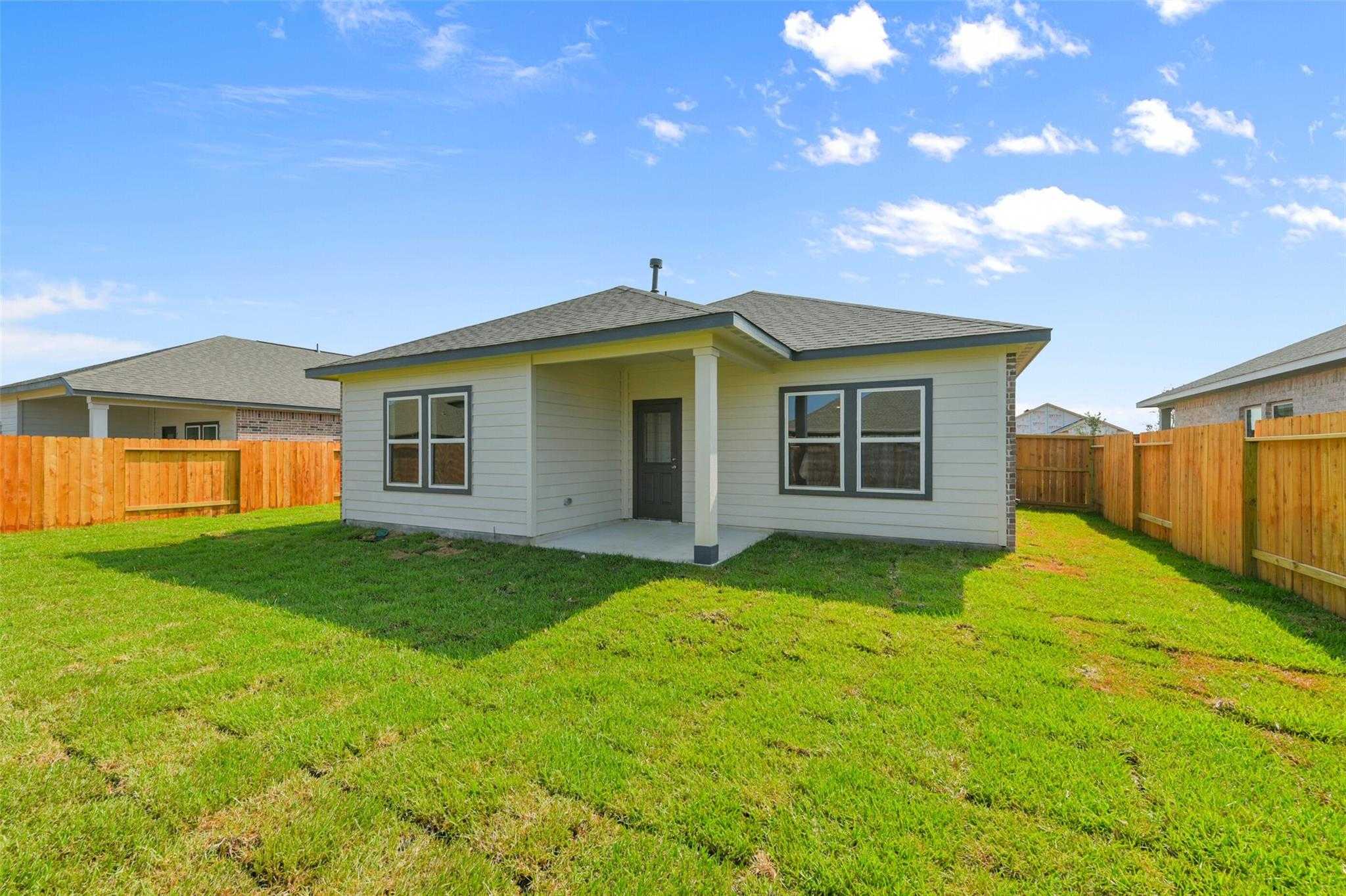 Single-story beige home with covered porch, double windows, and lush green lawn in River Ranch Meadows, Dayton, Texas