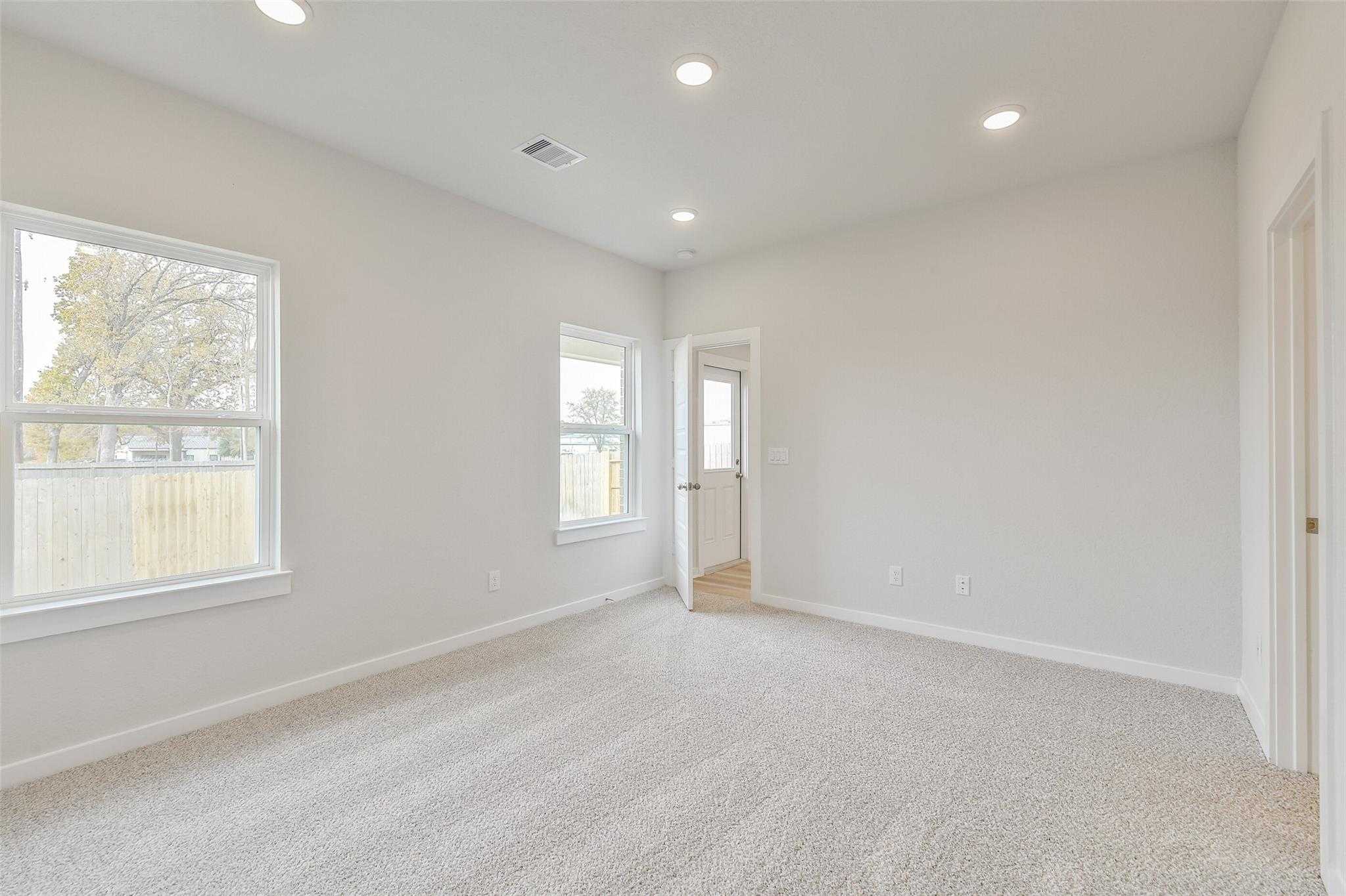 Spacious empty living room with beige carpet, walls, large windows, and recessed lights in Davidson Homes Colorado G, Magnolia TX