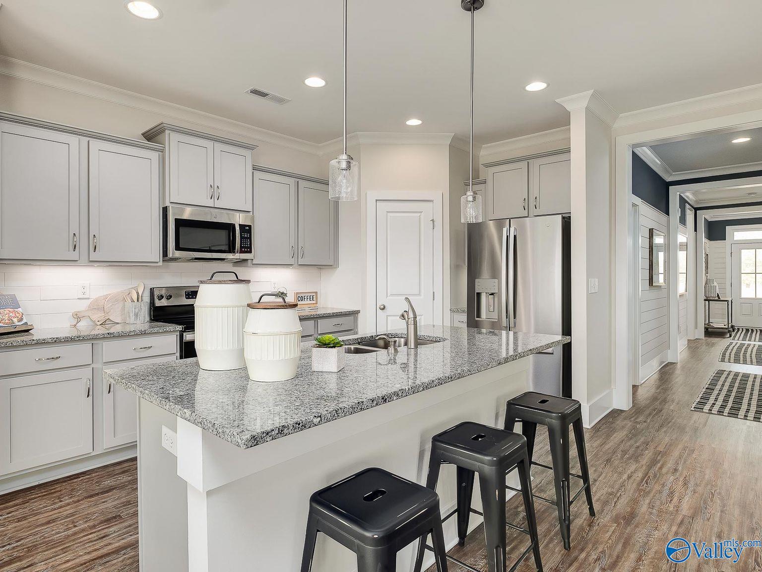 Modern white kitchen with granite island, stainless appliances, and bar stools in Davidson Homes The Everett, Toney, Alabama