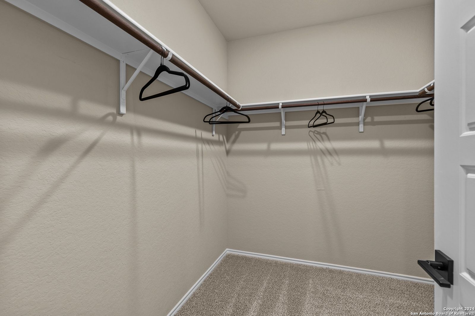 Spacious walk-in closet with wooden hanging rods, neutral beige walls, and carpet in Davidson Homes The Douglas F, Bricewood, San Antonio