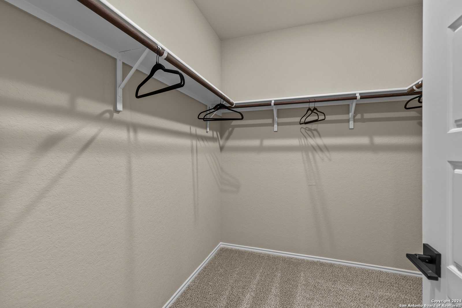 Spacious walk-in closet with wooden hanging rods, neutral beige walls, and carpet in Davidson Homes The Douglas F, Bricewood, San Antonio