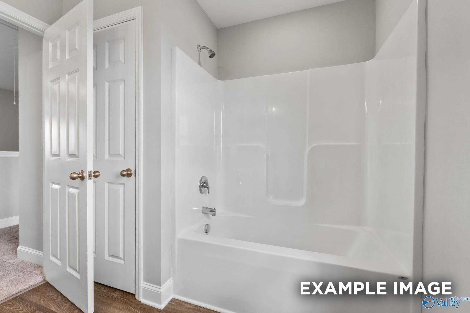 Modern bathroom featuring white tub-shower combo with glass doors in Davidson Homes The Shelby B, Athens, Alabama