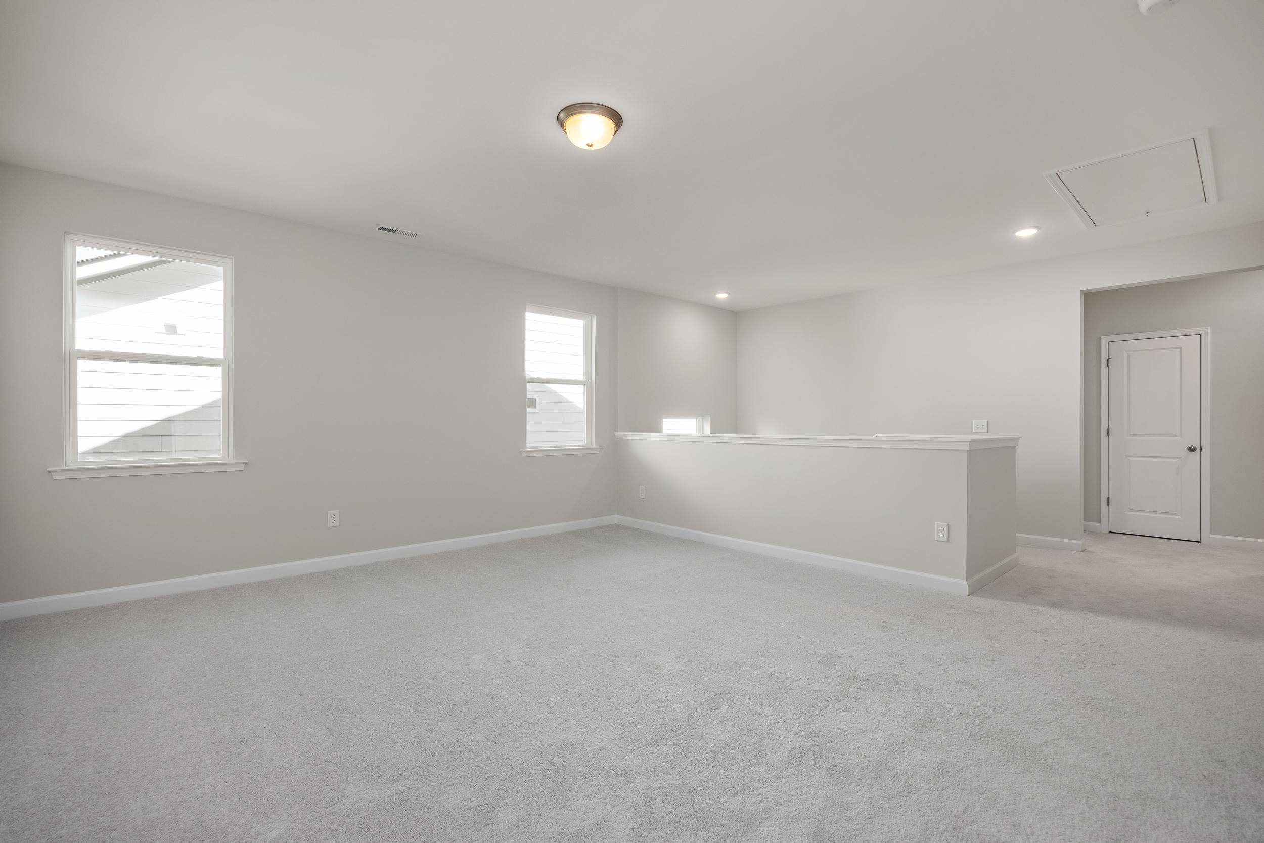 Spacious upstairs loft in The Aspen C home with gray carpet, large windows, balcony railing, and neutral walls