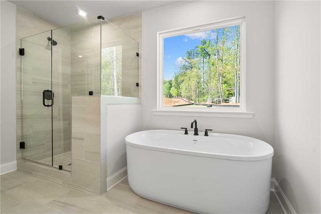 Elegant master bathroom with frameless glass shower, freestanding soaking tub, and tree-view window in Davidson Homes The Hickory B, Buford, GA