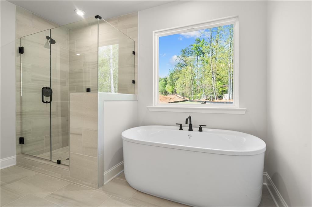 Elegant master bathroom with frameless glass shower, freestanding soaking tub, and wooded view window in The Hickory E, Buford, GA