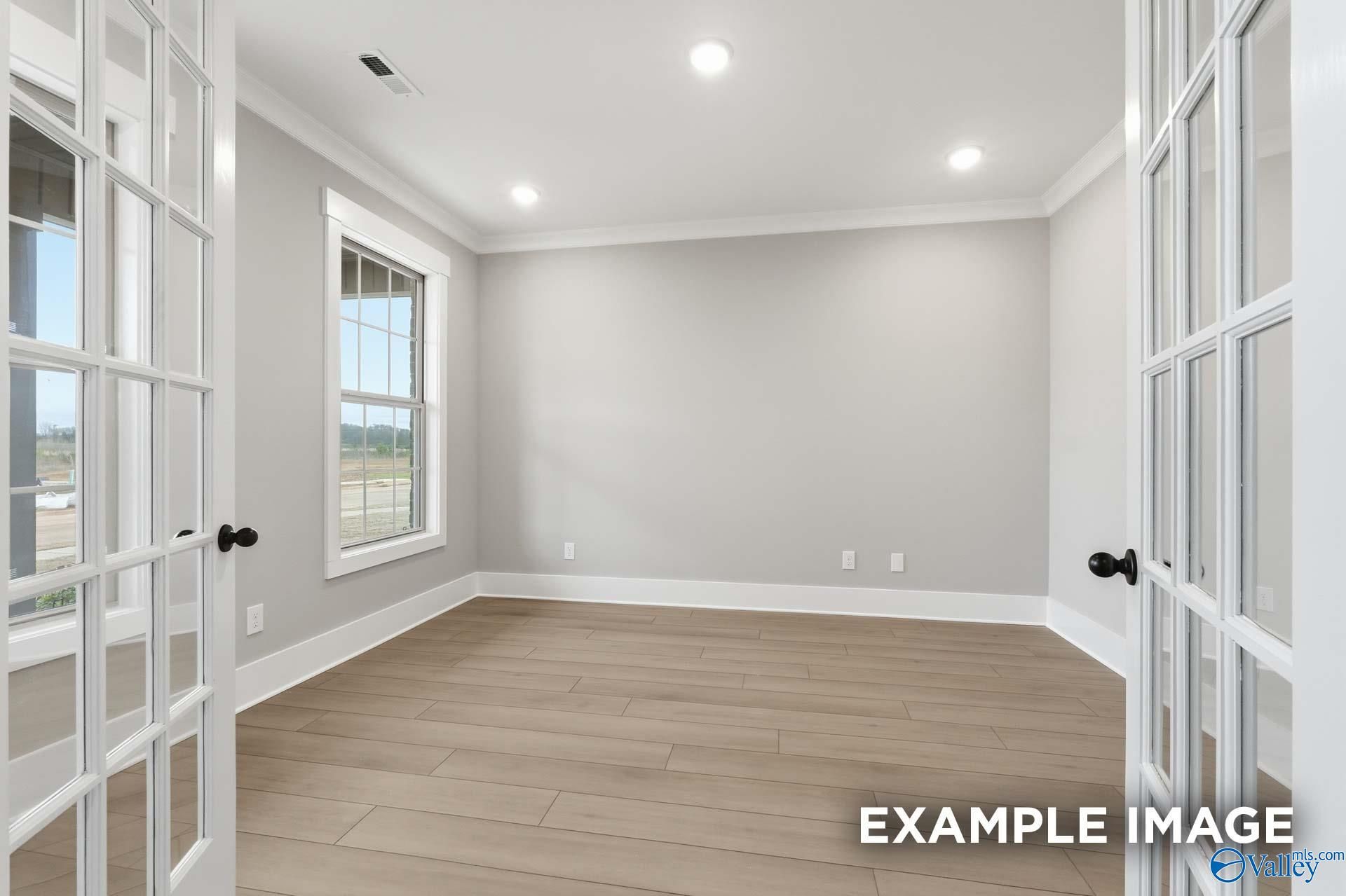 Bright empty room with light gray walls, hardwood floors, large window, and open French doors in Davidson Homes The Emory, Decatur, Alabama