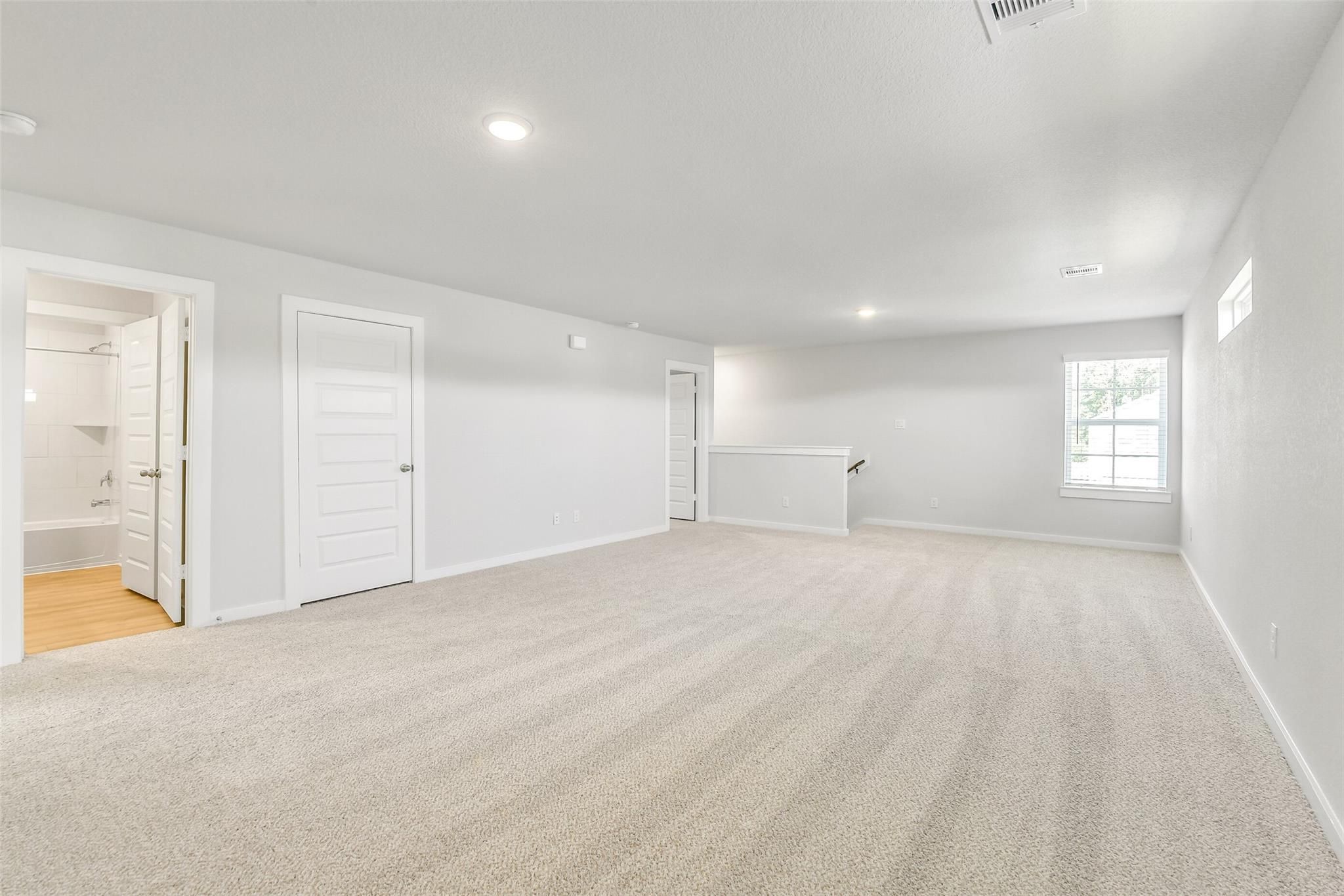 Spacious upstairs loft with beige carpet, white walls, adjacent bathroom, and window in 5-bedroom Davidson Homes The San Marcos E, Cleveland, Texas