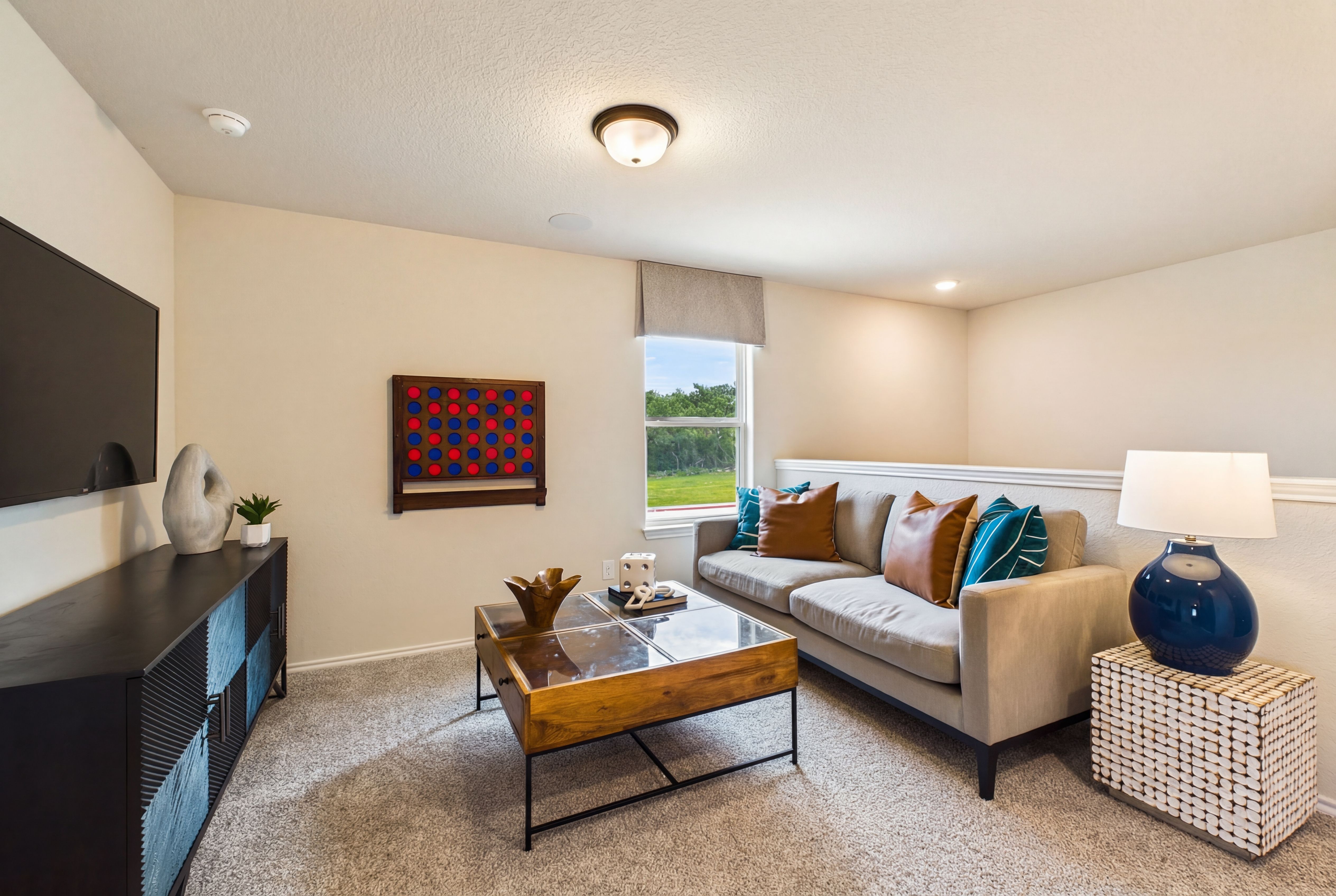Cozy living room at Meadows at Oak Creek in San Antonio TX with gray sofa, TV console, abstract art, and window views