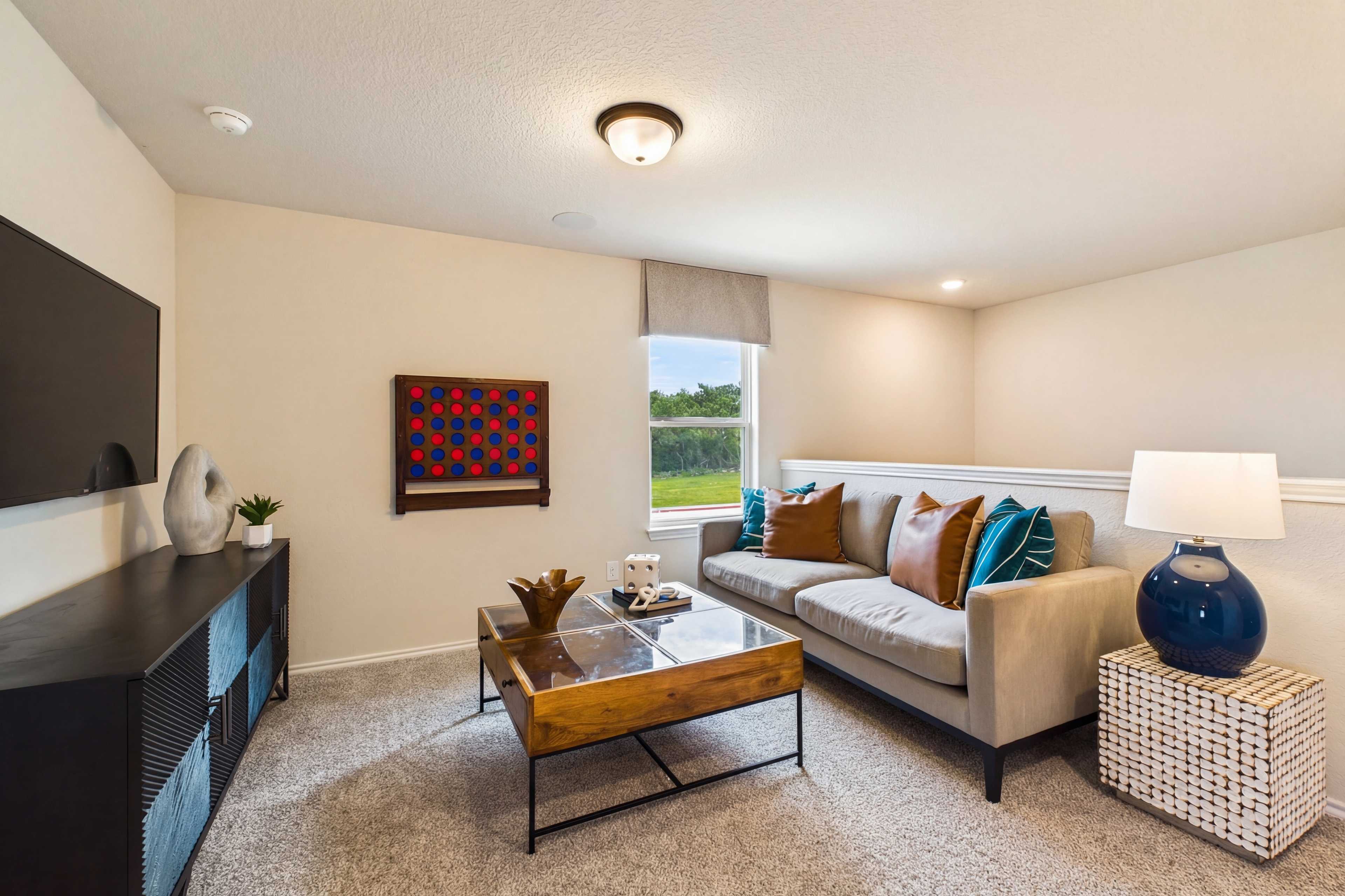 Cozy living room at Meadows at Oak Creek in San Antonio TX with gray sofa, TV console, abstract art, and window views