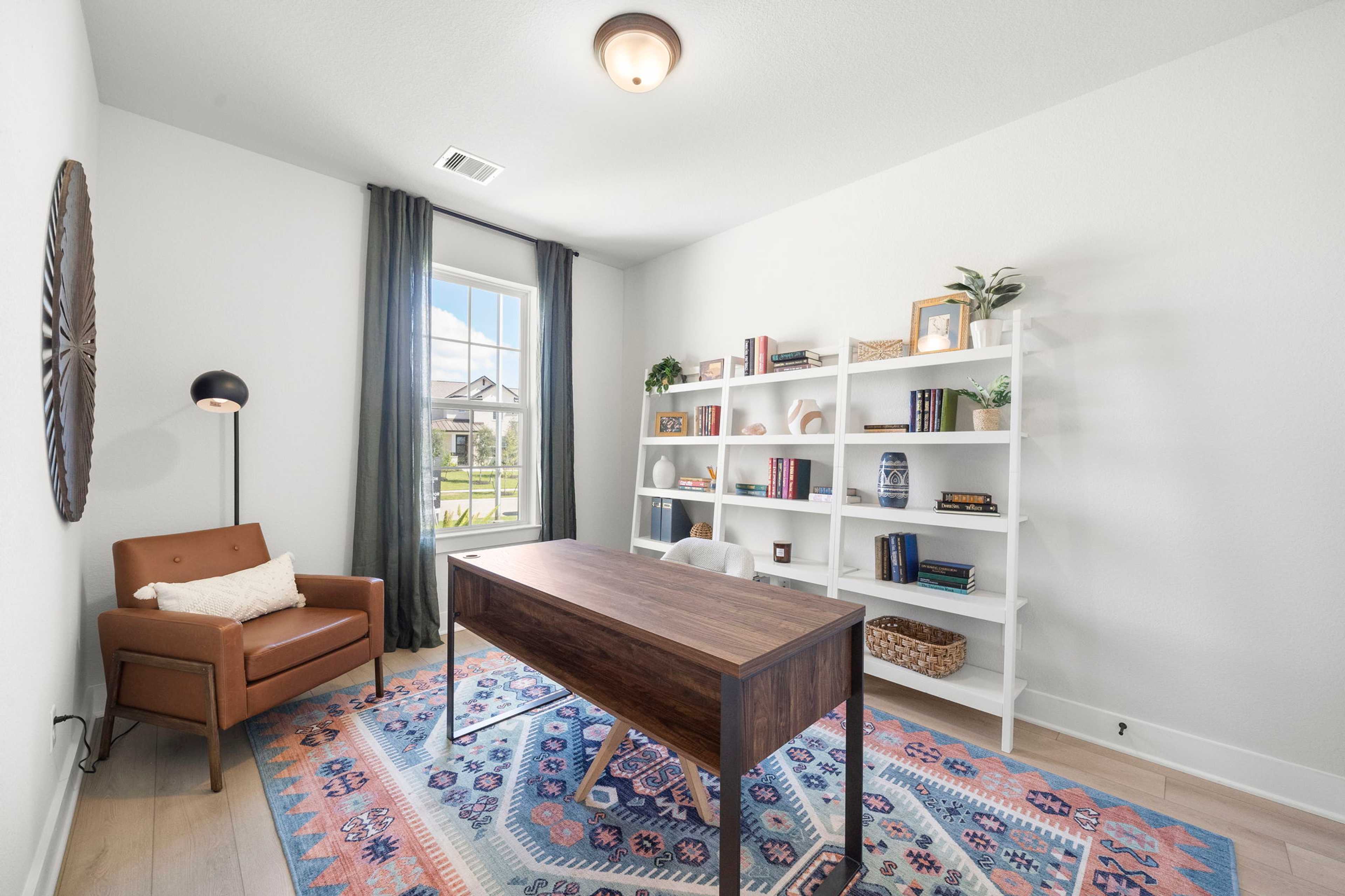 Cozy home office at Lago Mar in Texas City, Texas by Davidson Homes with wooden desk, white bookshelves, leather armchair, and large window