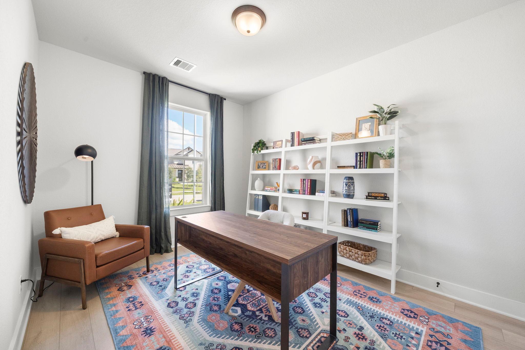 Cozy home office at Lago Mar in Texas City, Texas by Davidson Homes with wooden desk, white bookshelves, leather armchair, and large window