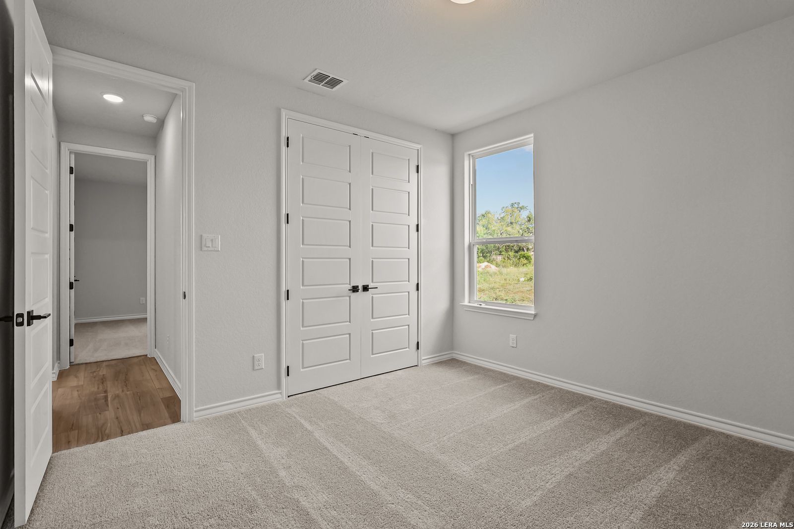 Bright carpeted bedroom with white double closet doors and window in Davidson Homes The Oxford F, Potranco Oaks, Castroville, TX