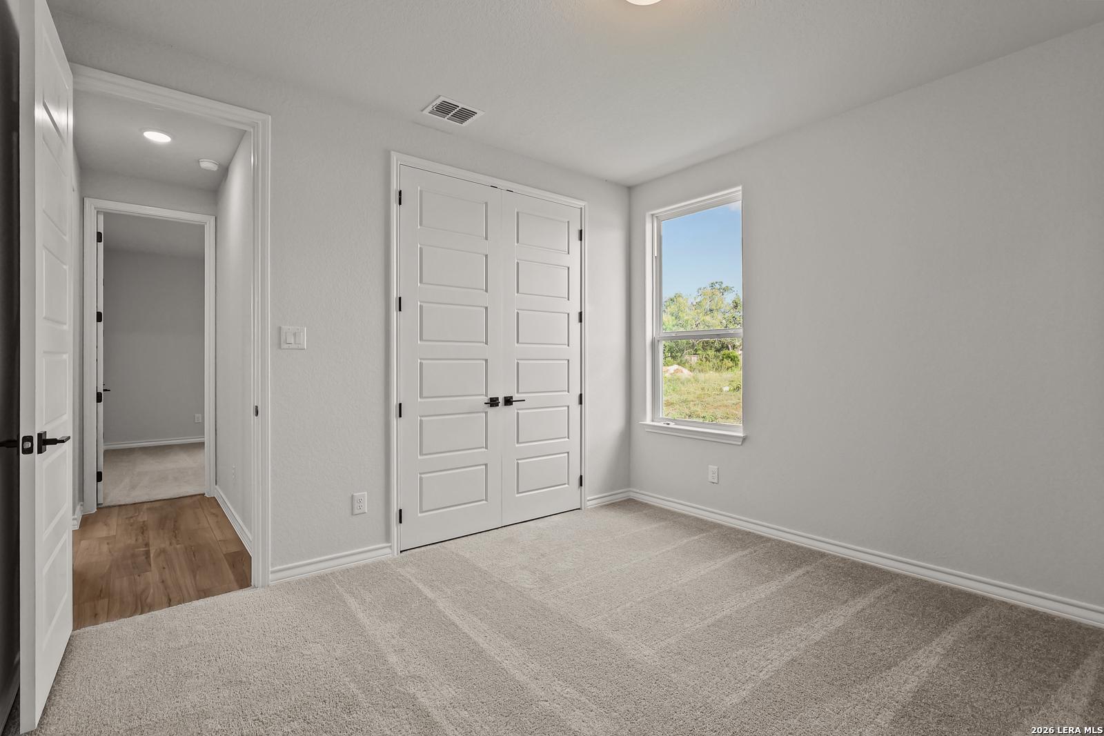 Bright carpeted bedroom with white double closet doors and window in Davidson Homes The Oxford F, Potranco Oaks, Castroville, TX