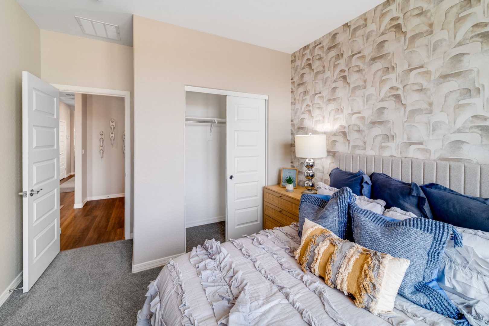 Spacious master bedroom in The Newport B showcasing king bed with blue pillows, open walk-in closet, and en-suite bath