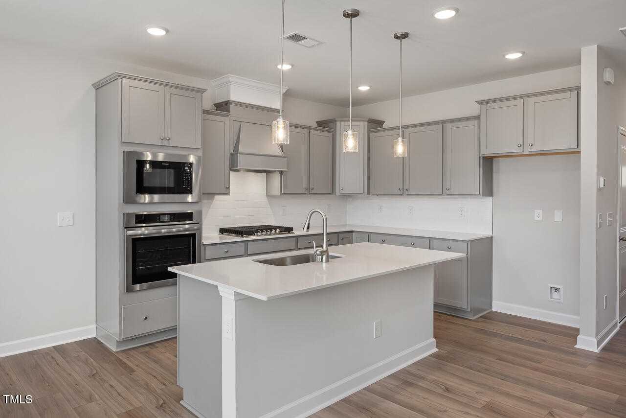 Contemporary gray shaker kitchen with center island sink, stainless appliances, pendant lights in Davidson Homes The Graham, Fuquay-Varina, NC