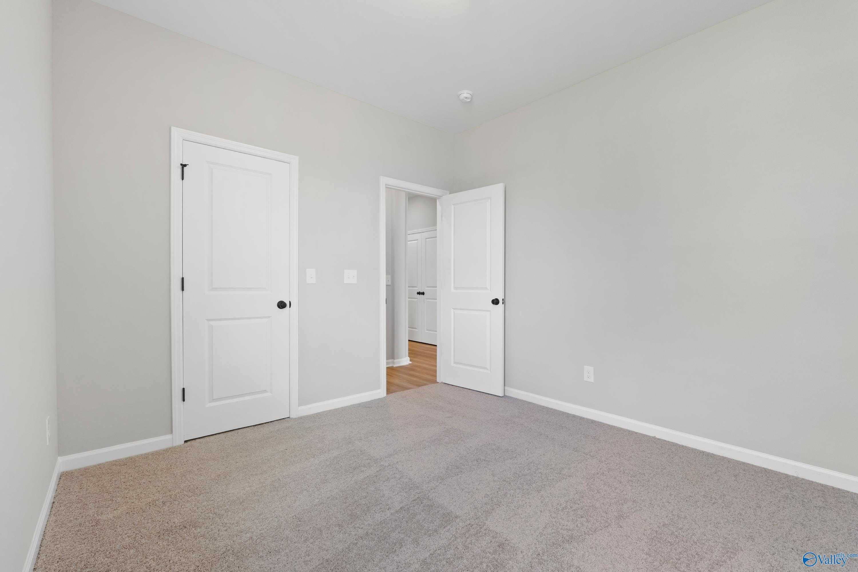 Bright bedroom featuring gray walls, beige carpet, white doors to bathroom in The Nantucket by Evermore Homes, Madison AL