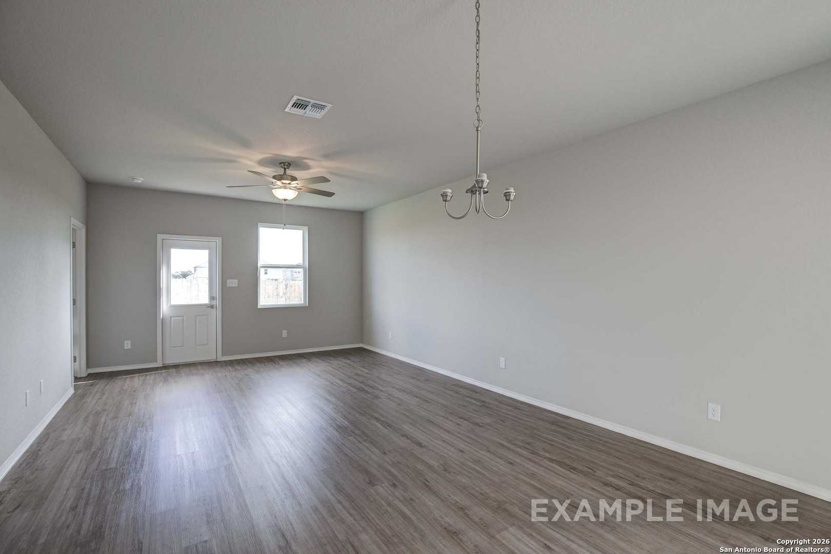 Spacious empty living room with hardwood floors, ceiling fan, and chandelier in Davidson Homes The Frio B, San Antonio