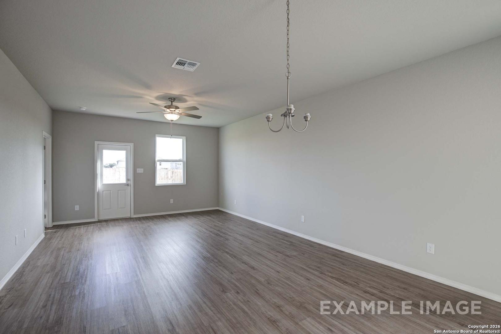 Spacious empty living room with hardwood floors, ceiling fan, chandelier, and large windows in Davidson Homes The Frio C, Agave, San Antonio