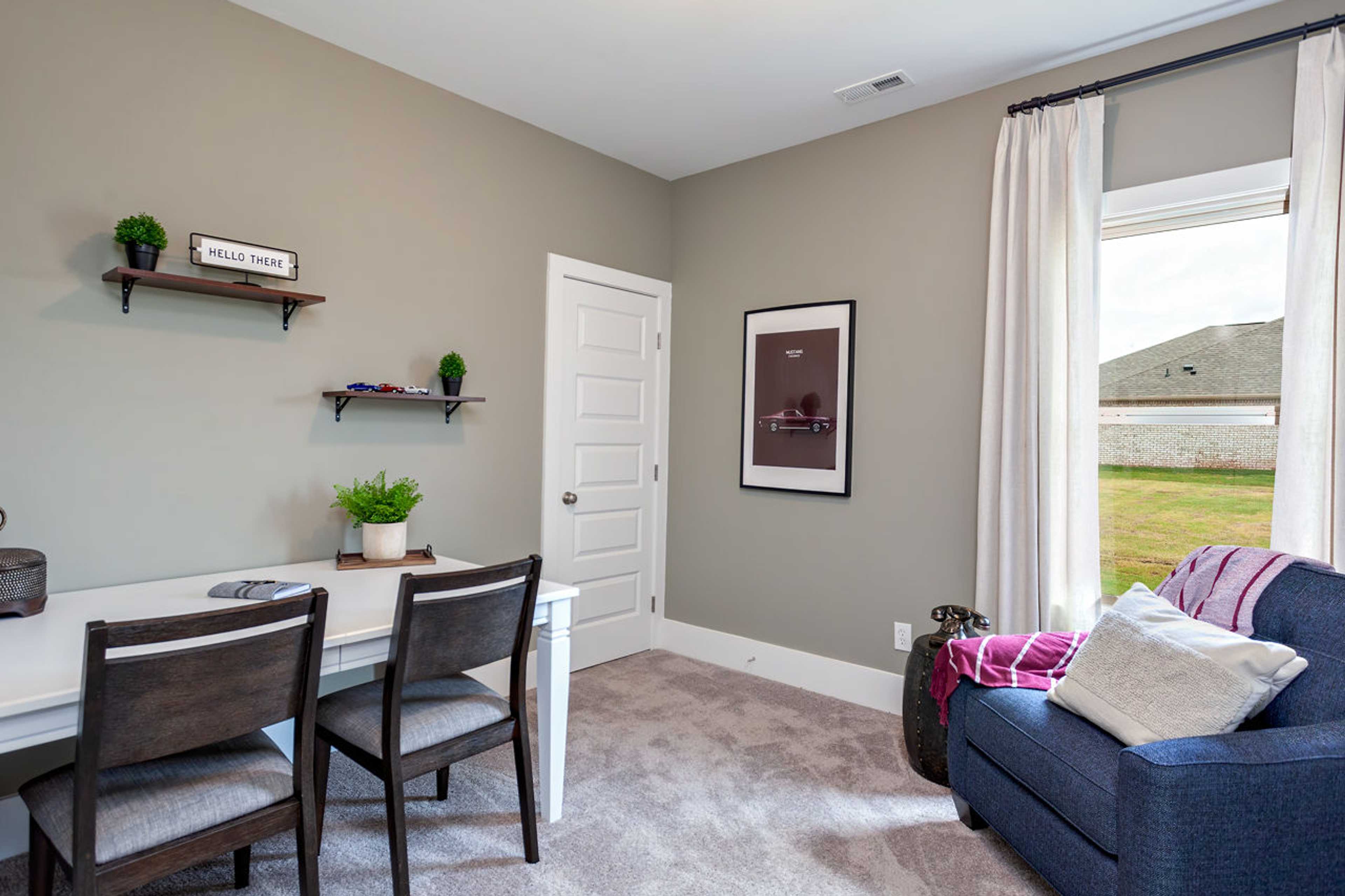 Cozy home office in Williams Pointe Huntsville AL with wooden desk, potted plants, blue armchair, and window overlooking green lawn