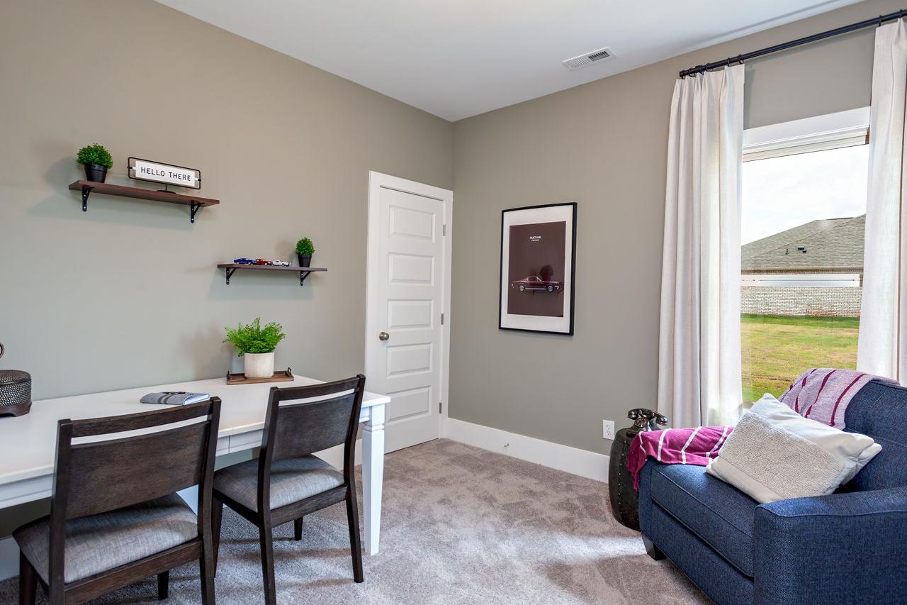 Cozy home office in Williams Pointe Huntsville AL with wooden desk, potted plants, blue armchair, and window overlooking green lawn