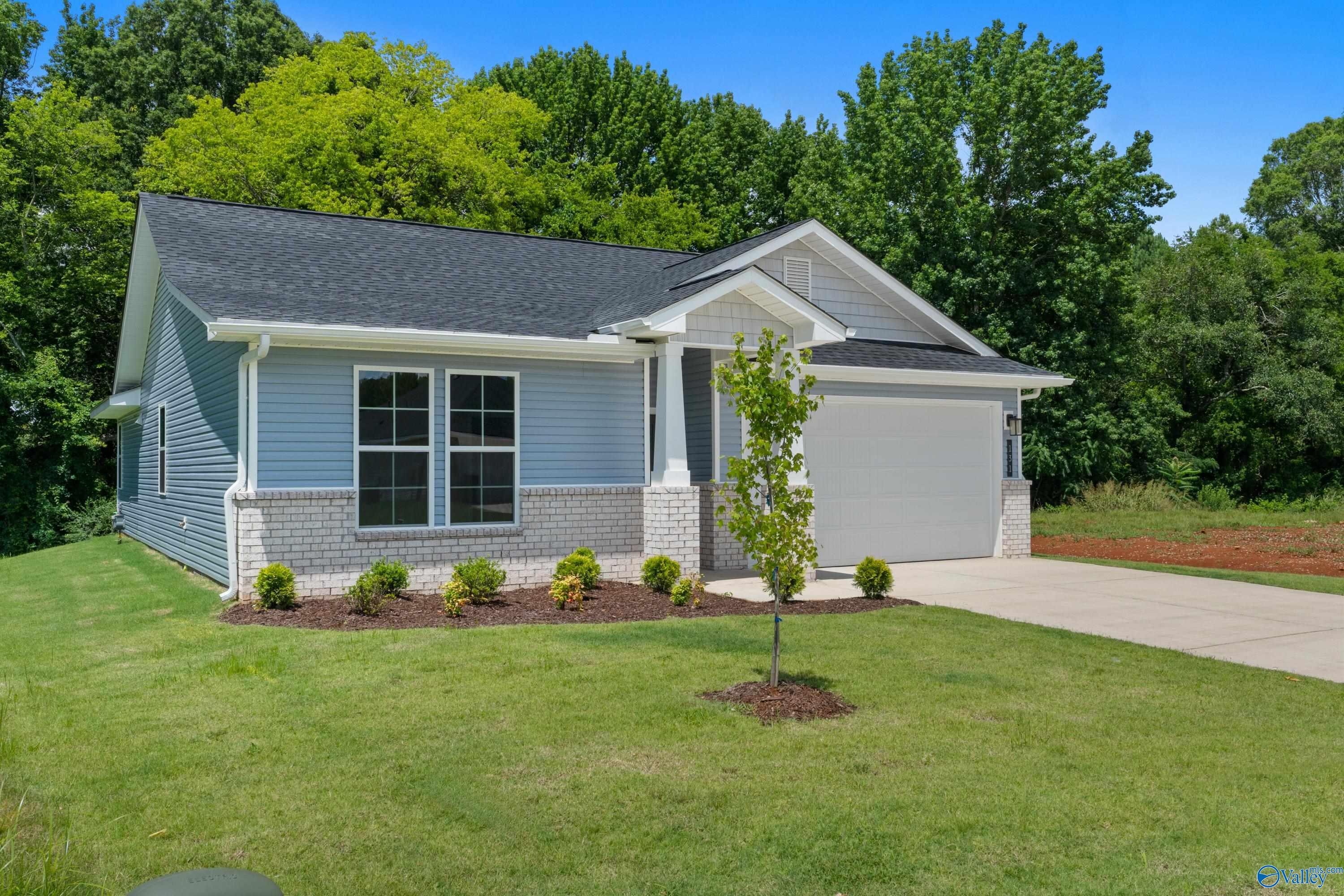 Light blue single-story 3-bedroom home with 2-car garage, front porch, and lush green landscaping in Forest Glen, Hazel Green, Alabama by Davidson Homes The Phoenix