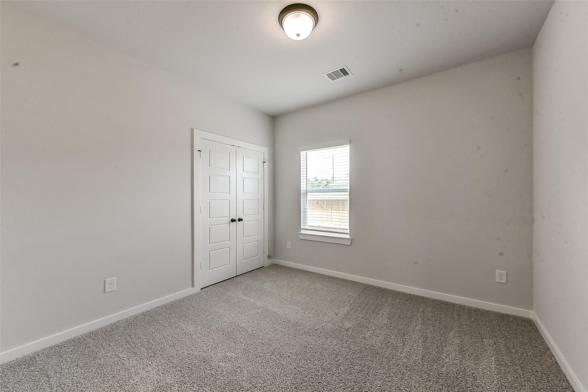 Bright secondary bedroom featuring light gray walls, white bi-fold closet, window blinds, and neutral carpet in Davidson Homes Everett C, Crosby TX