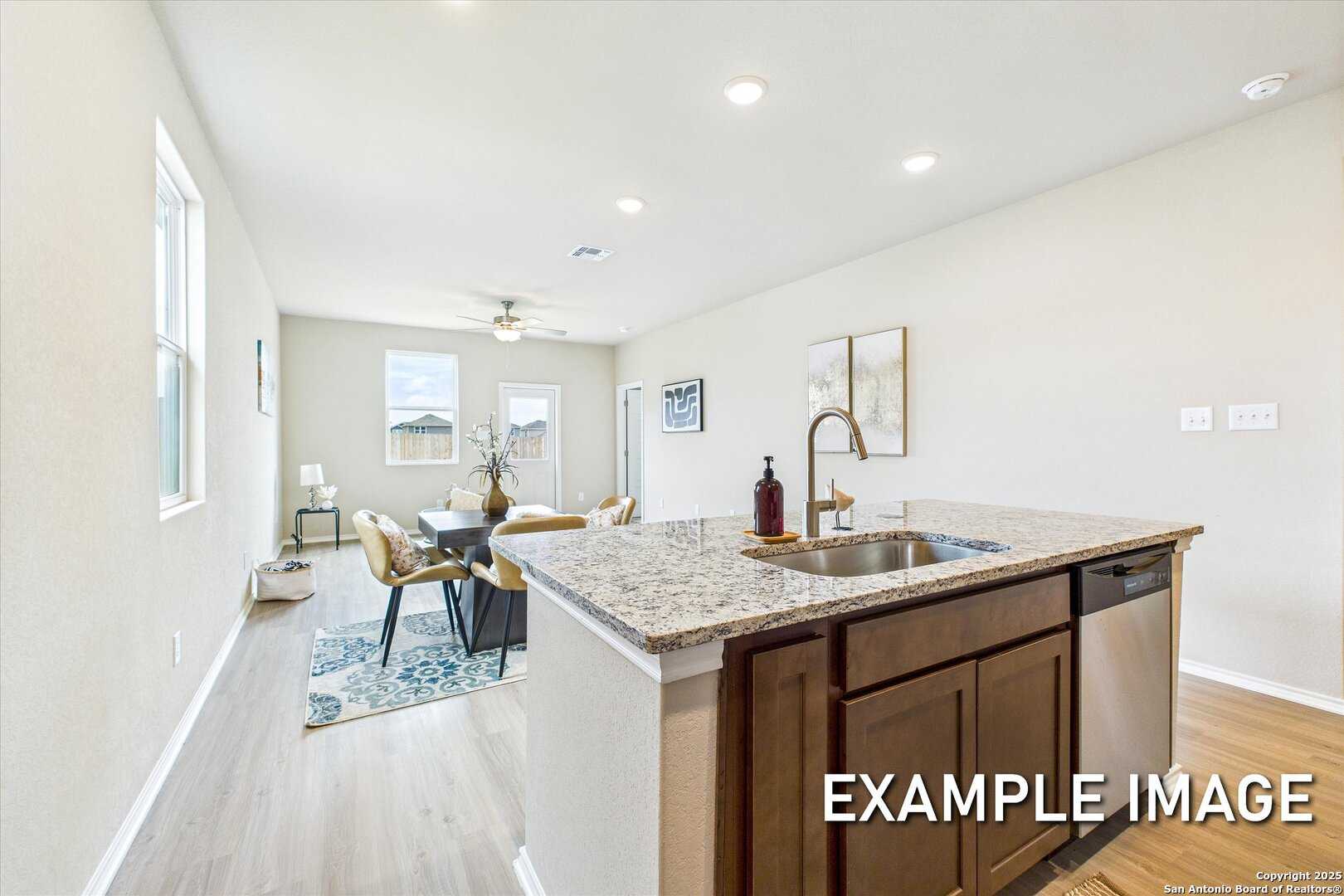 Open-concept kitchen and living room with granite island, stainless sink, wood cabinets, and beige sofa in Davidson Homes The Comal B, San Antonio