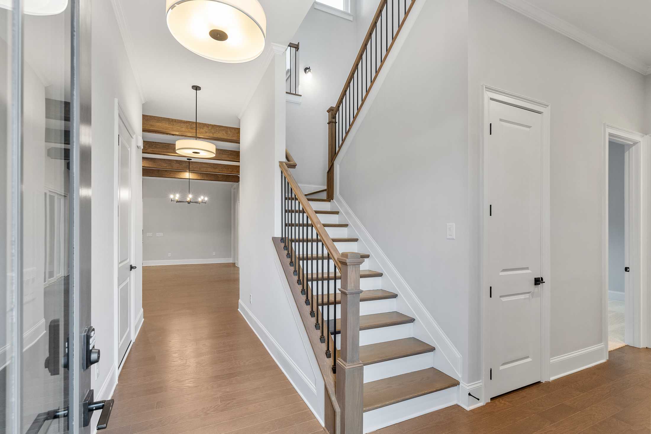 Spacious hallway in The Seaside home design with grand wooden staircase, wrought iron railing, hardwood floors, and pendant lighting