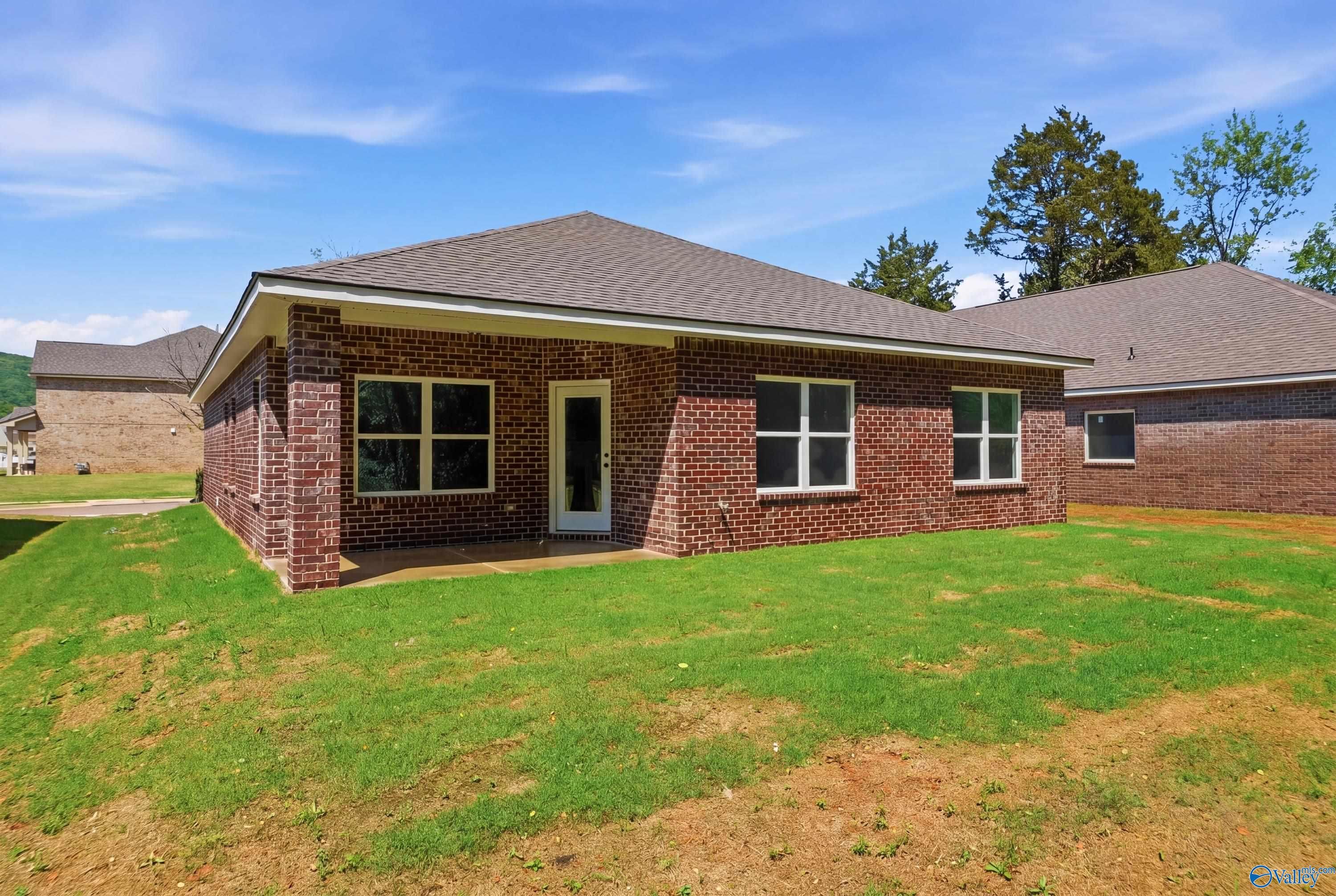 Red brick single-story home with gabled shingle roof, double windows, white door, and covered porch on lush green lawn in Jaguar Hills, Huntsville Alabama