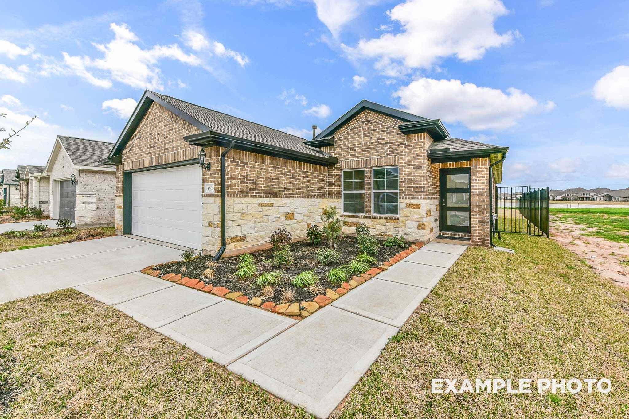 Modern brick and stone facade of The Costa B 1-story home featuring 2-car garage, landscaped driveway, and Texas blue sky