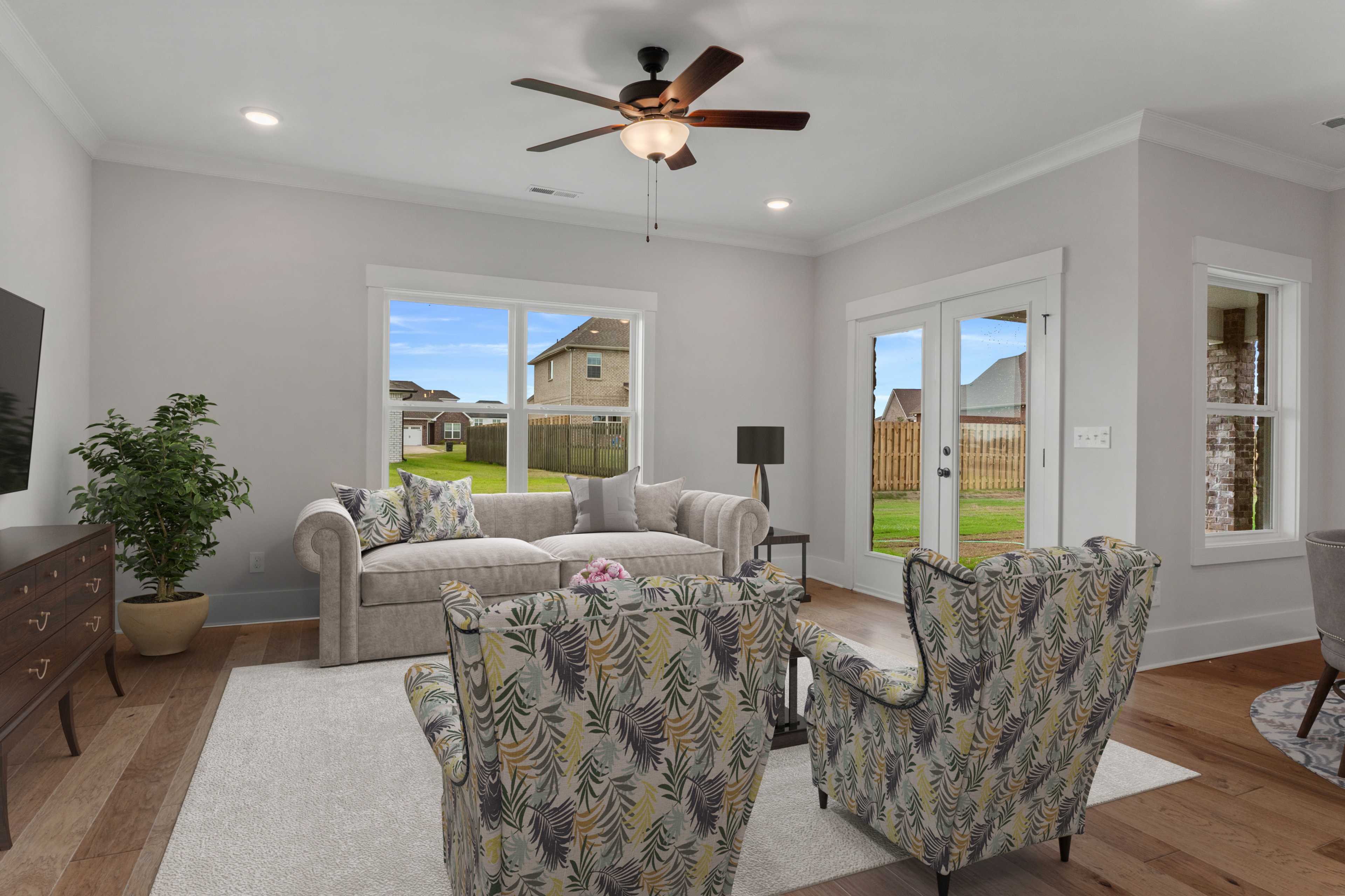 Bright living room at The Villas at Barnett's Crossing in Madison Alabama with beige sofa, leaf-patterned armchairs, hardwood floors, and large backyard windows
