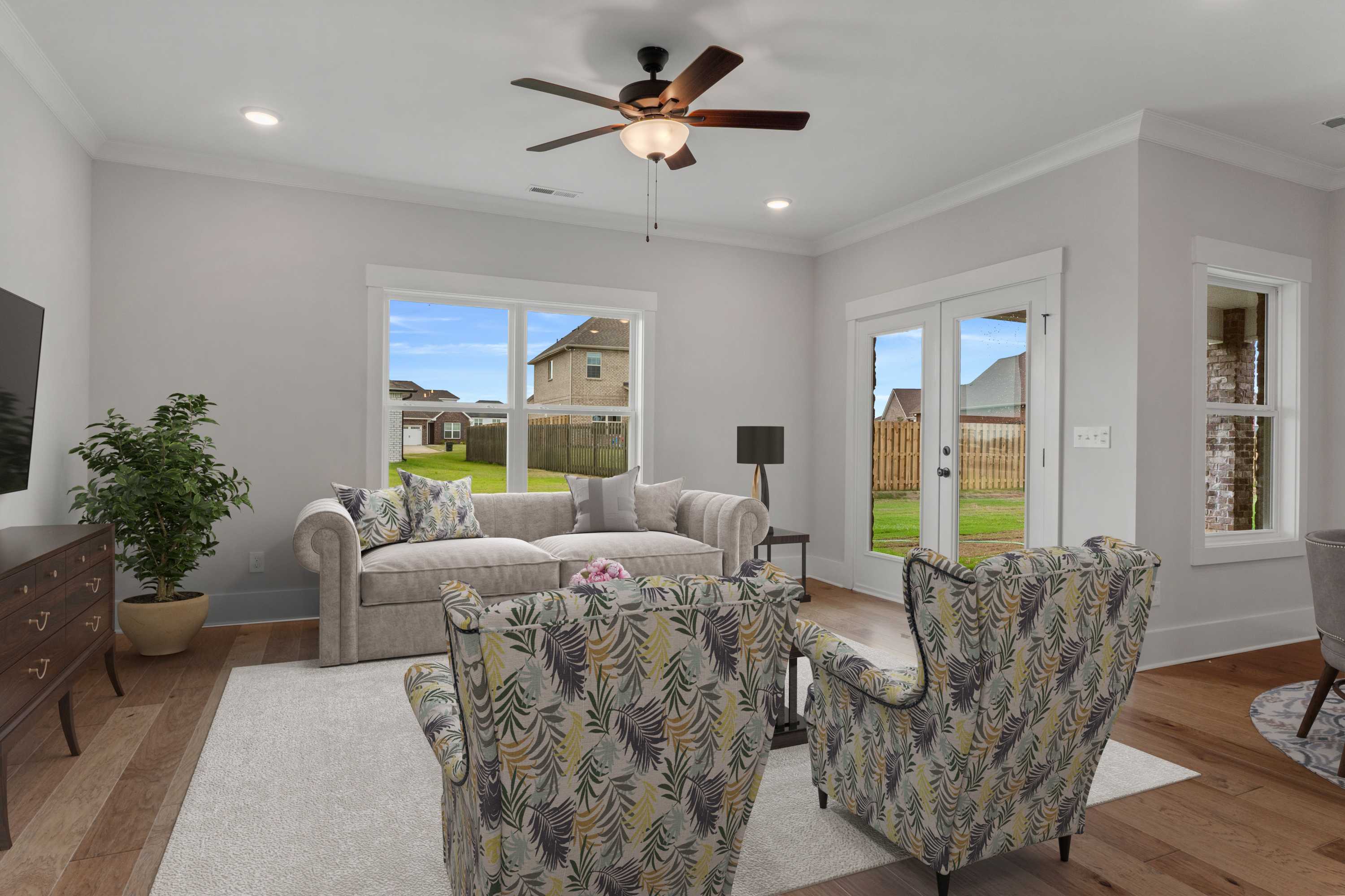 Bright living room at The Villas at Barnett's Crossing in Madison Alabama with beige sofa, leaf-patterned armchairs, hardwood floors, and large backyard windows