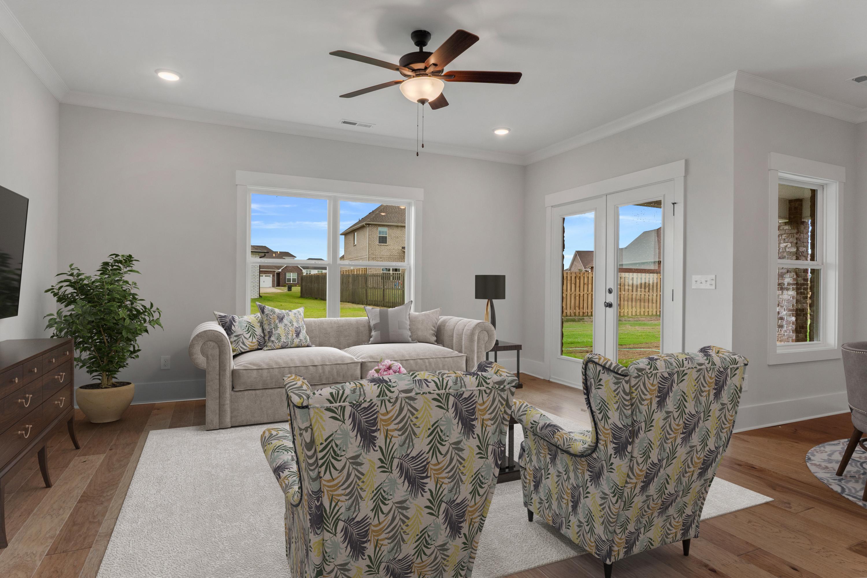 Bright living room at The Villas at Barnett's Crossing in Madison Alabama with beige sofa, leaf-patterned armchairs, hardwood floors, and large backyard windows