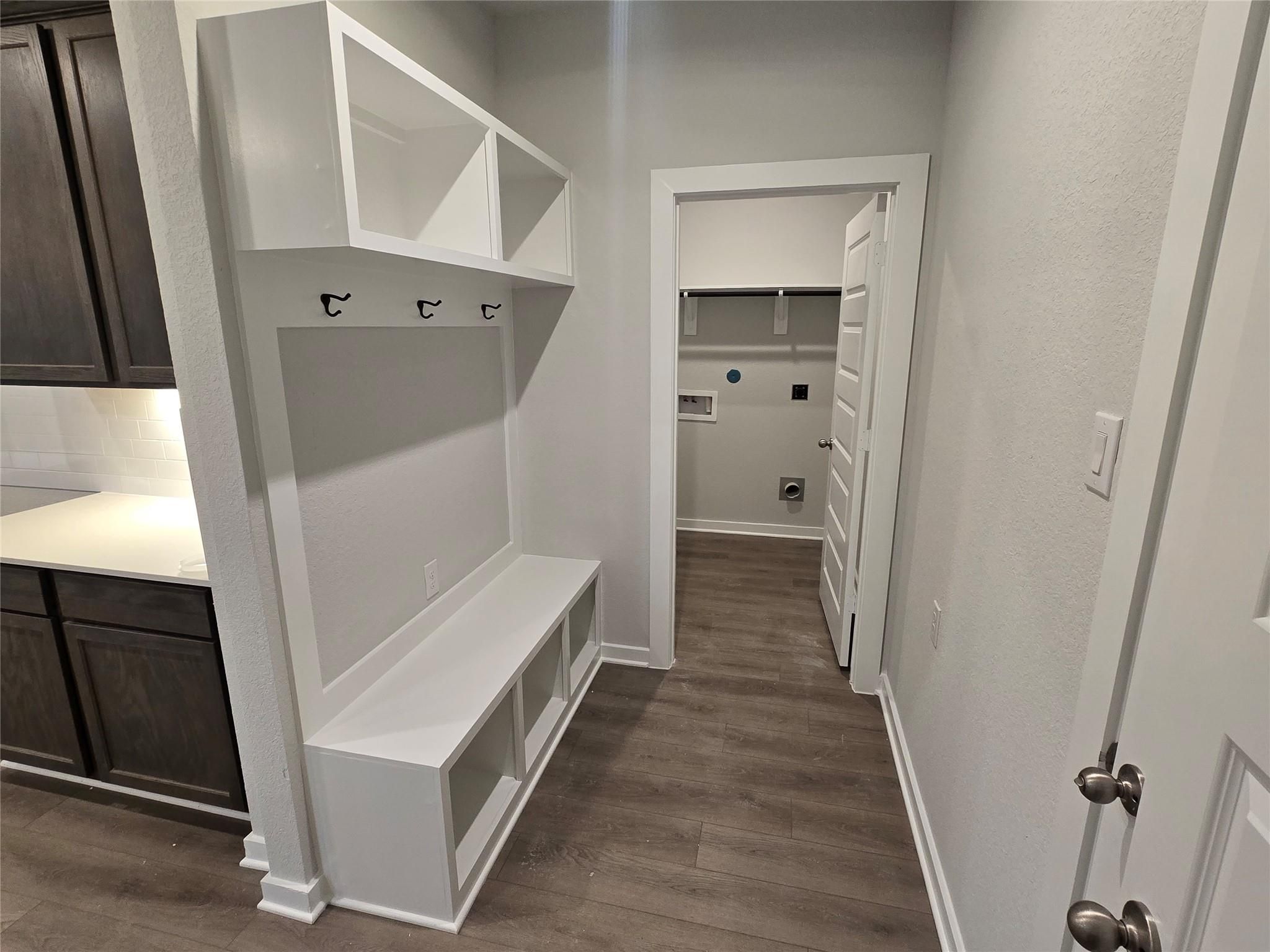Functional mudroom with white built-in cabinets, coat hooks, storage bench, and laundry room access in Davidson Homes The Brazos E, Cleveland, Texas