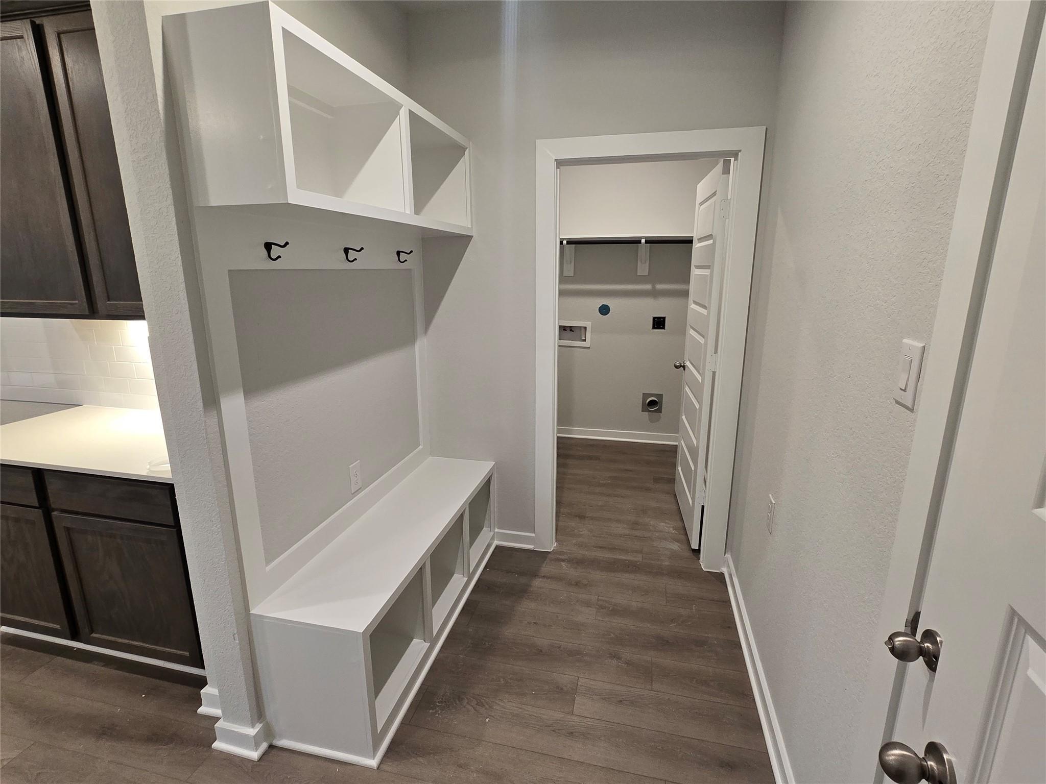 Functional mudroom with white built-in cabinets, coat hooks, storage bench, and laundry room access in Davidson Homes The Brazos E, Cleveland, Texas