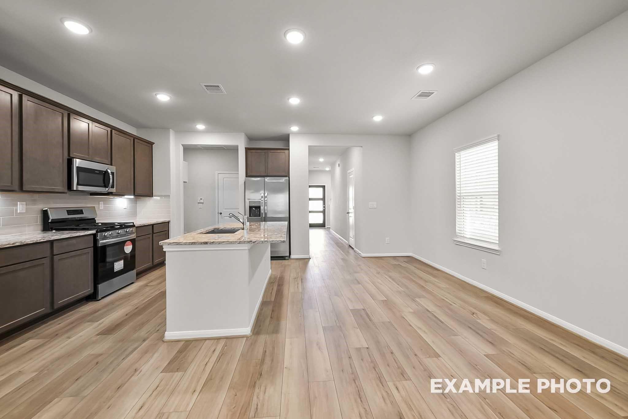 Open-concept kitchen with island and wood-style flooring in The Blanco F floor plan at Spring Branch Crossing, Conroe.
