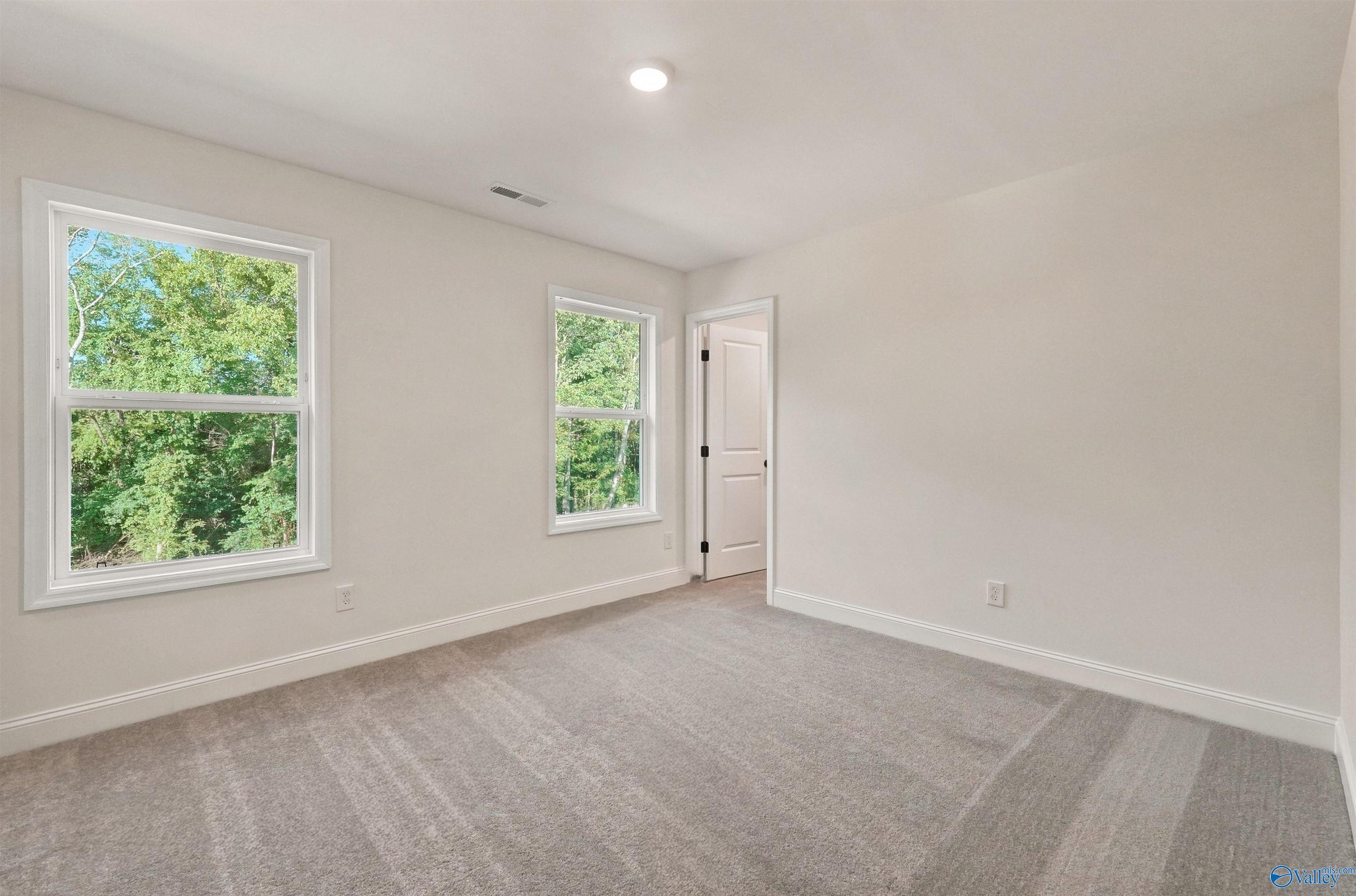 Bright, carpeted bedroom with large windows in The Chelsea C floor plan at Creek Grove, New Market, Alabama.