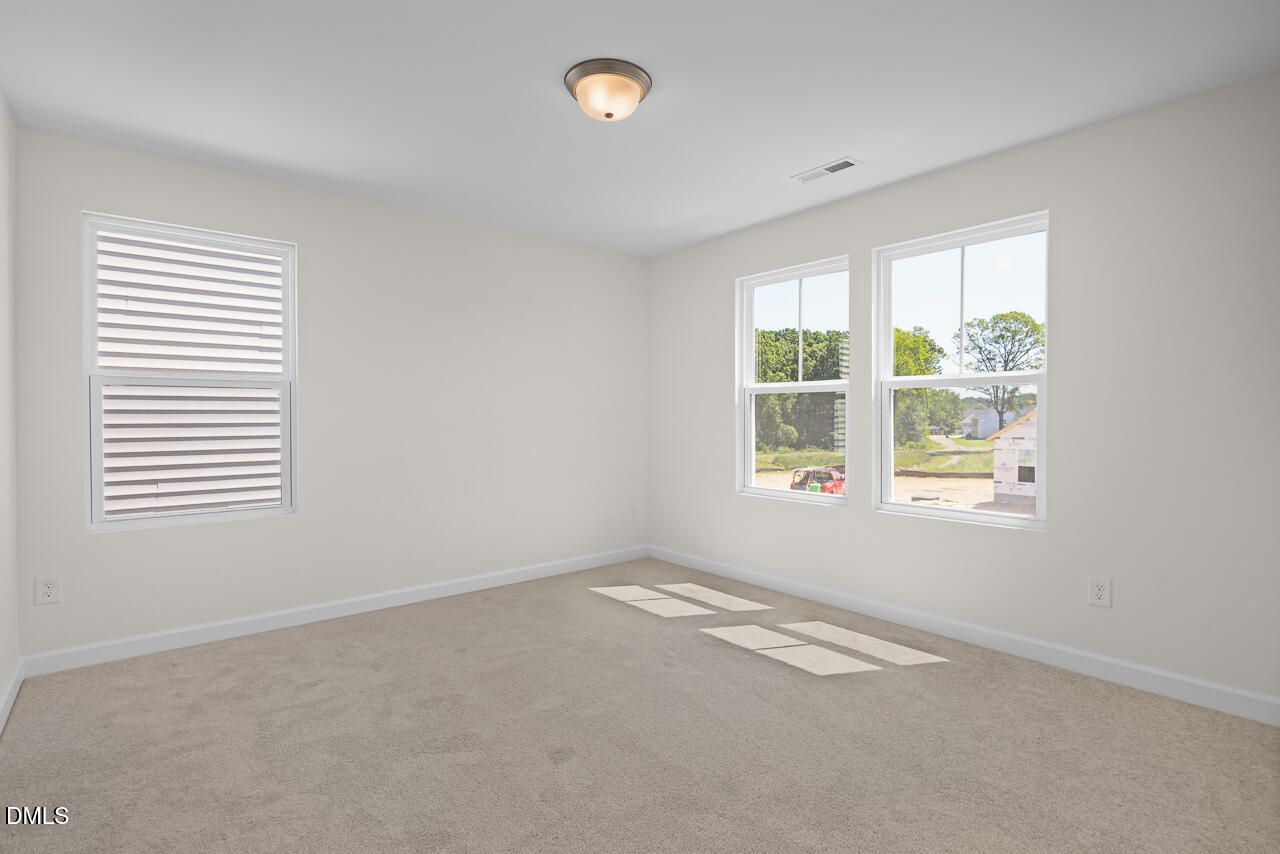 Bright, carpeted bedroom with white plantation shutters in Davidson Homes' The Willow B at Woodland Crossing, Zebulon NC