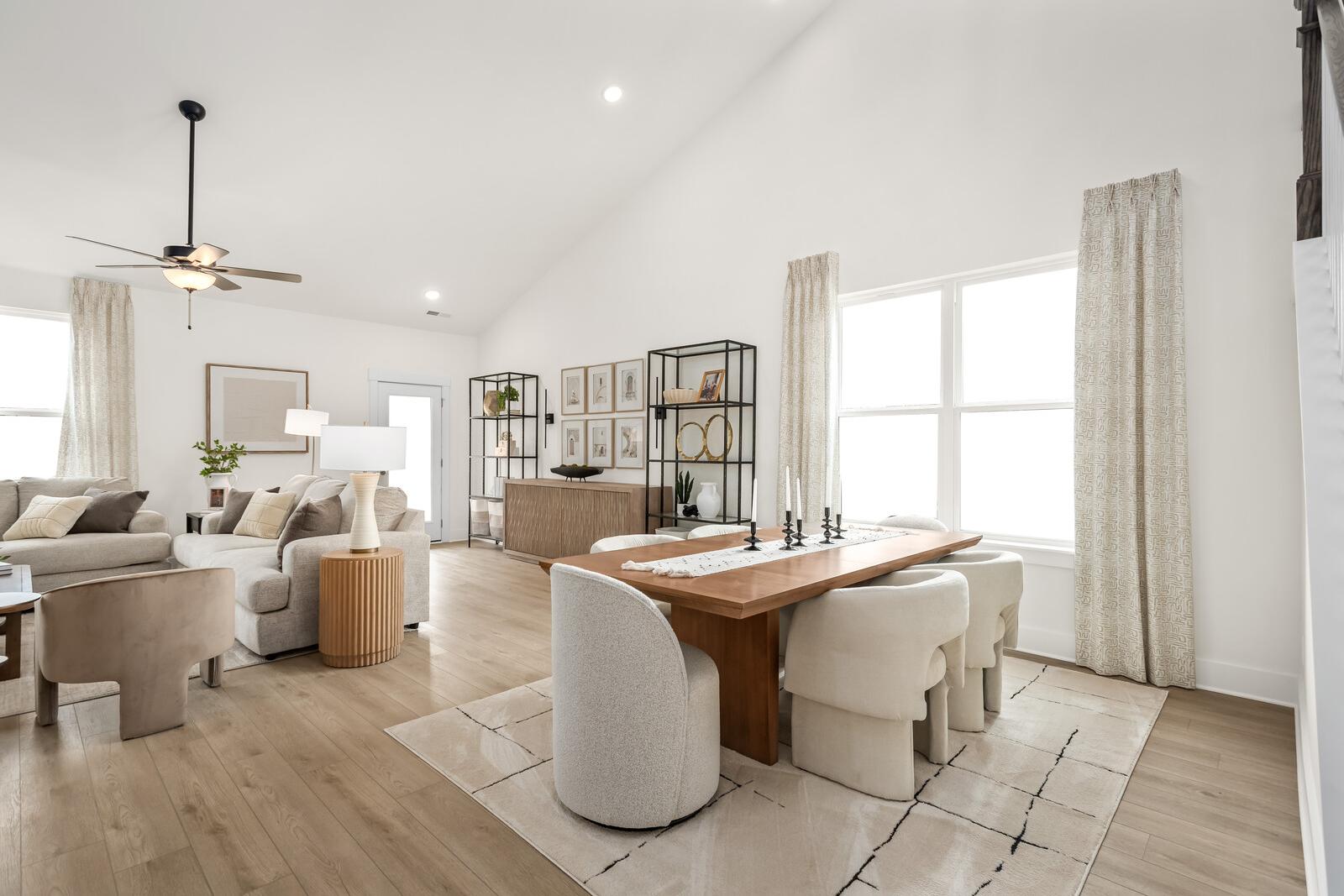 Spacious open-concept living and dining area in The Ridgeport home featuring high ceilings, neutral sectional sofa, wooden table with upholstered chairs, and large windows