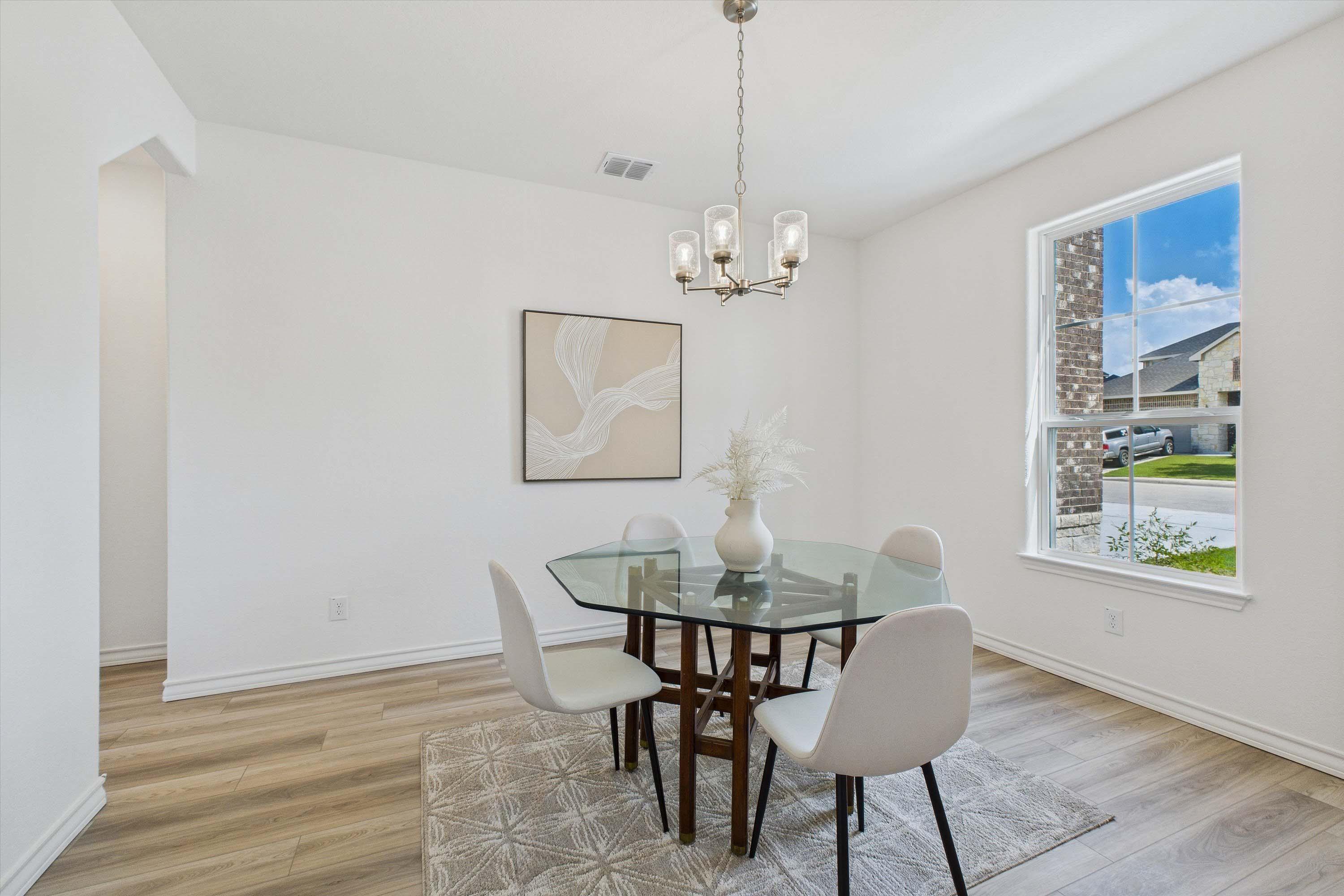 Bright dining area in The Danbury home design featuring a glass-top table, modern lighting, and wood-style flooring.